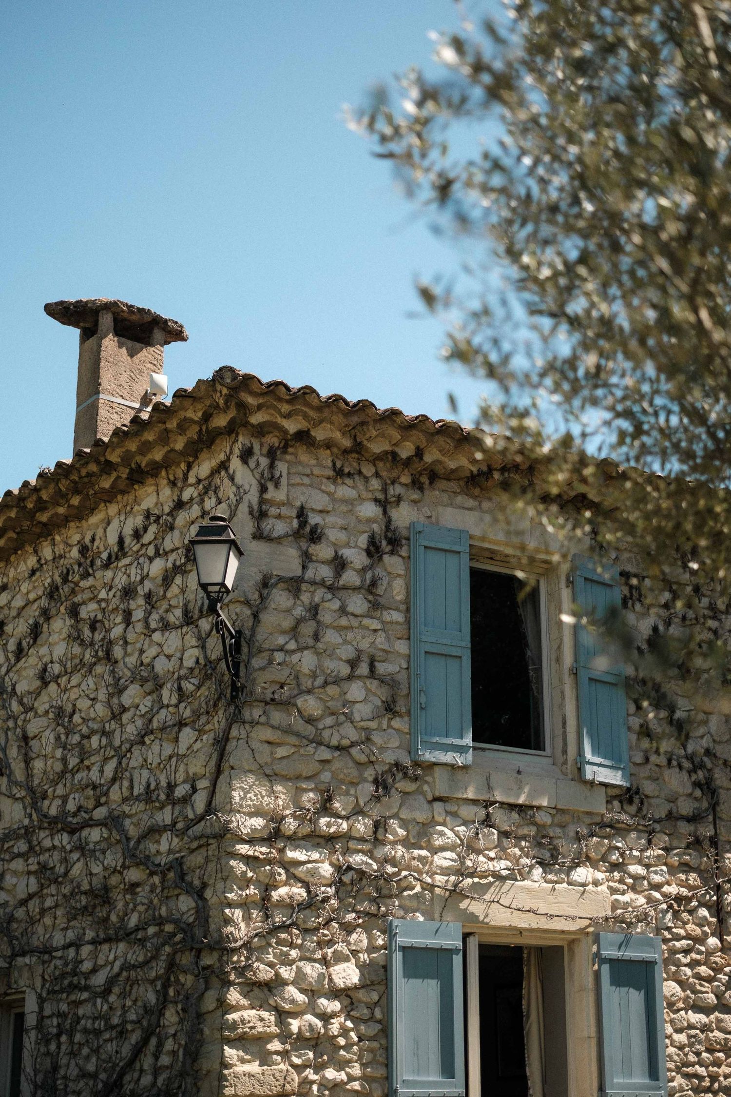Rustic stone house with blue shuttered windows and terracotta roof tiles in Mediterranean architectural style.