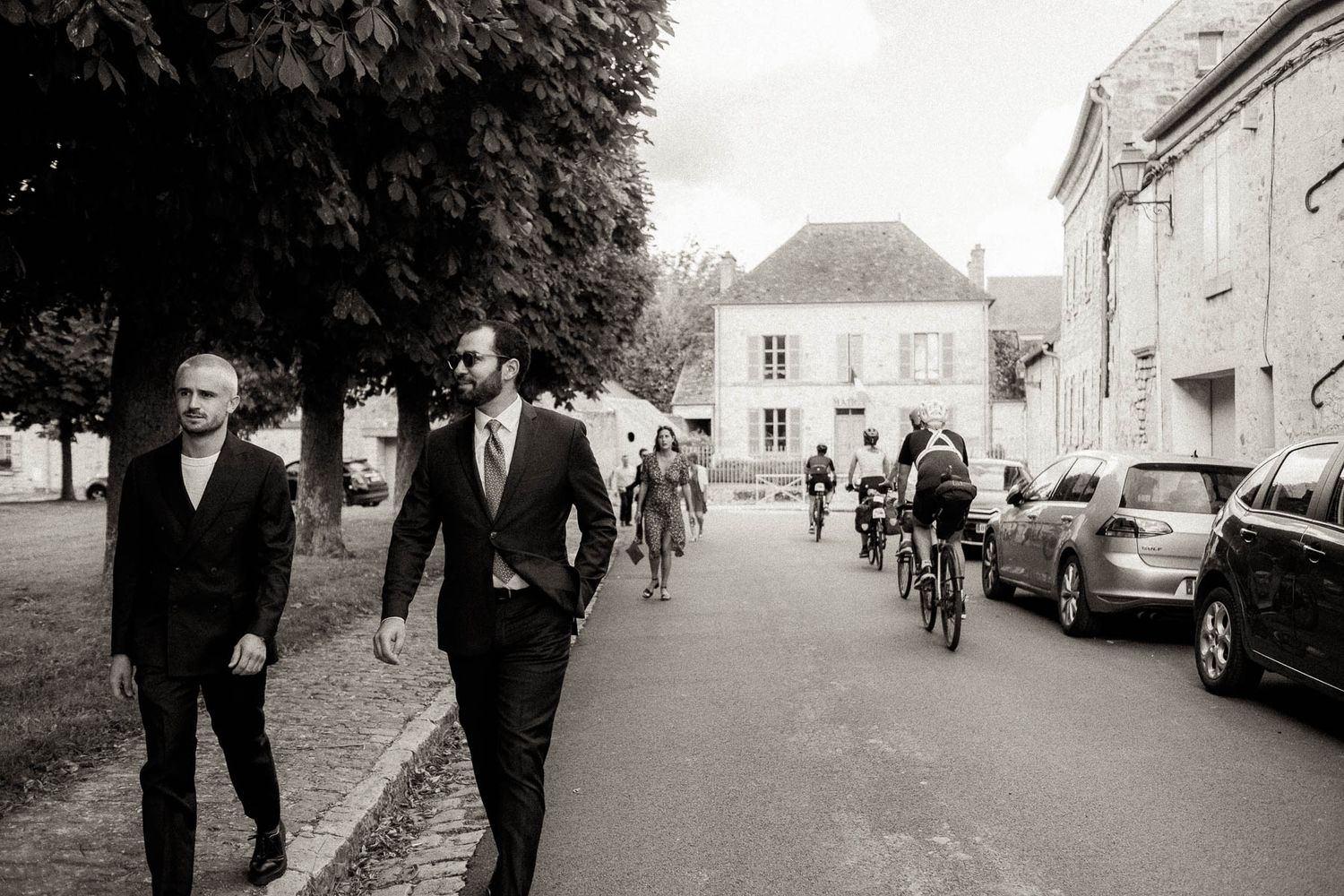A series of black and white wedding photographs showing guests walking and mingling outside a historic building.
