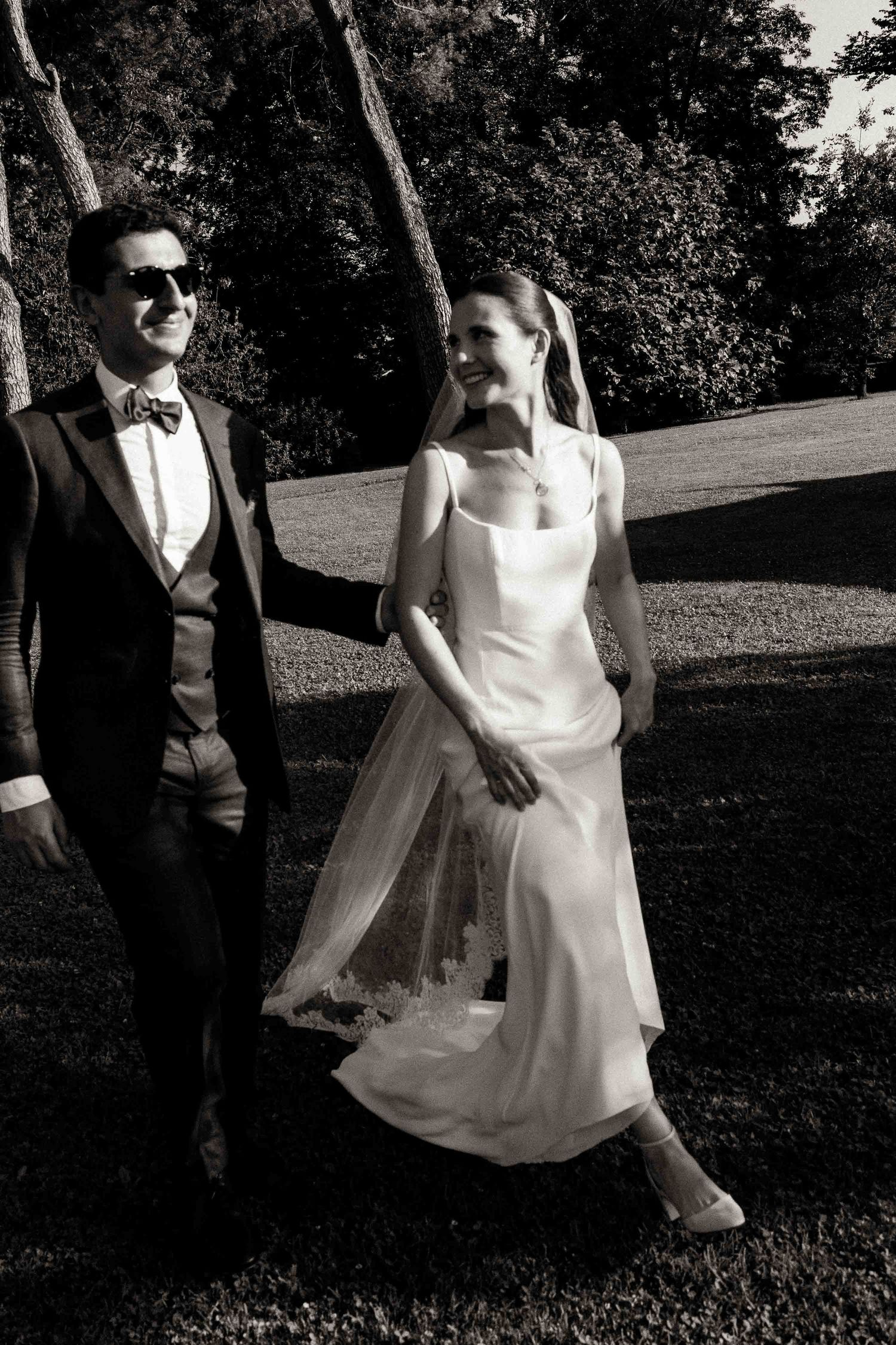 A couple in formal wedding attire dance and twirl together in an outdoor garden setting.