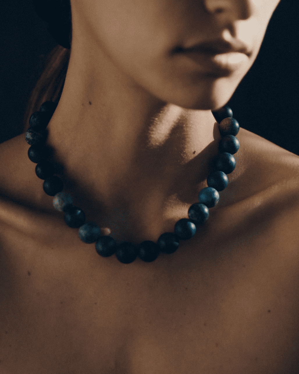A close-up view of a dark beaded necklace against bare skin in moody lighting.