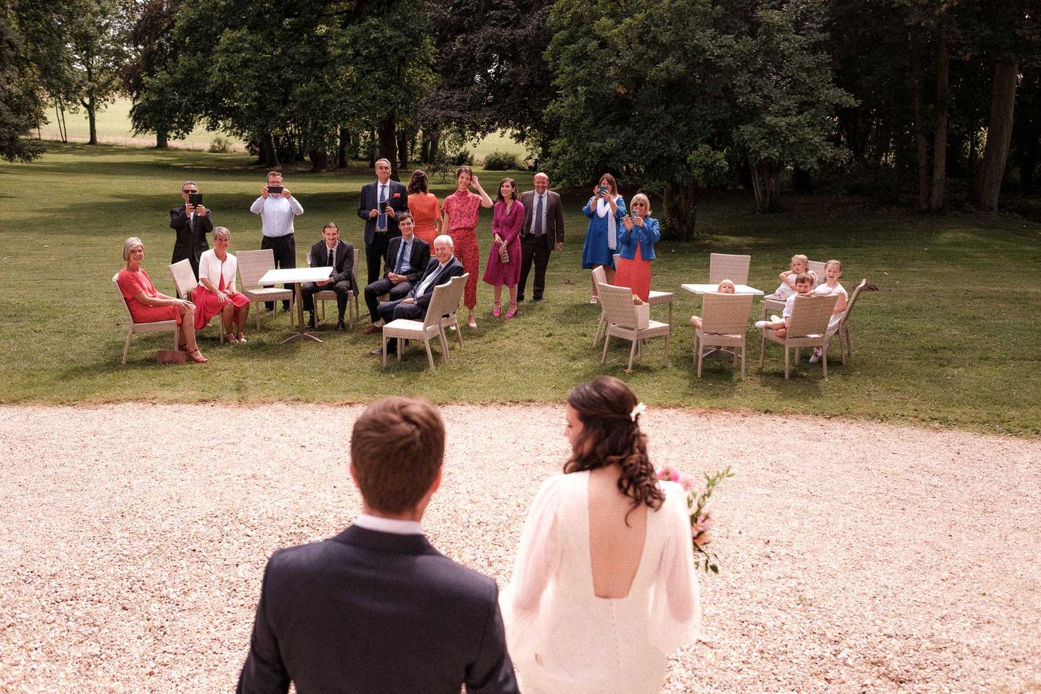Outdoor wedding ceremony setup with white chairs arranged in rows on a grassy lawn surrounded by trees.