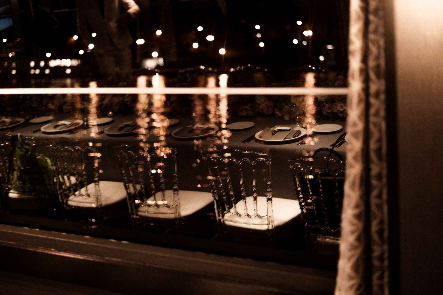 Empty wine glasses lined up on a dark windowsill with twinkling city lights visible in the reflection.