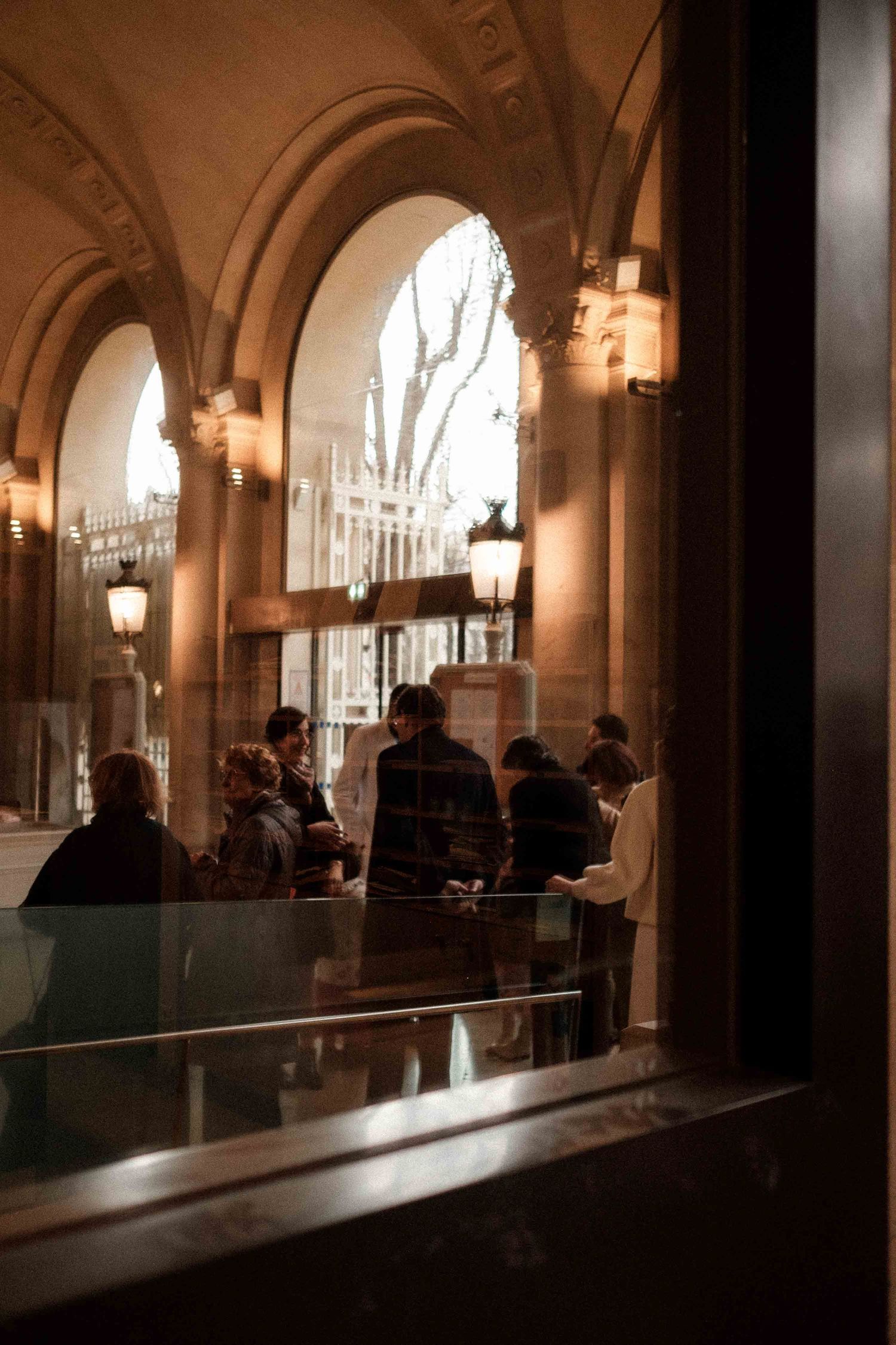 Elegant arched hallway with warm lighting and silhouettes of people gathered in a classical architectural setting.