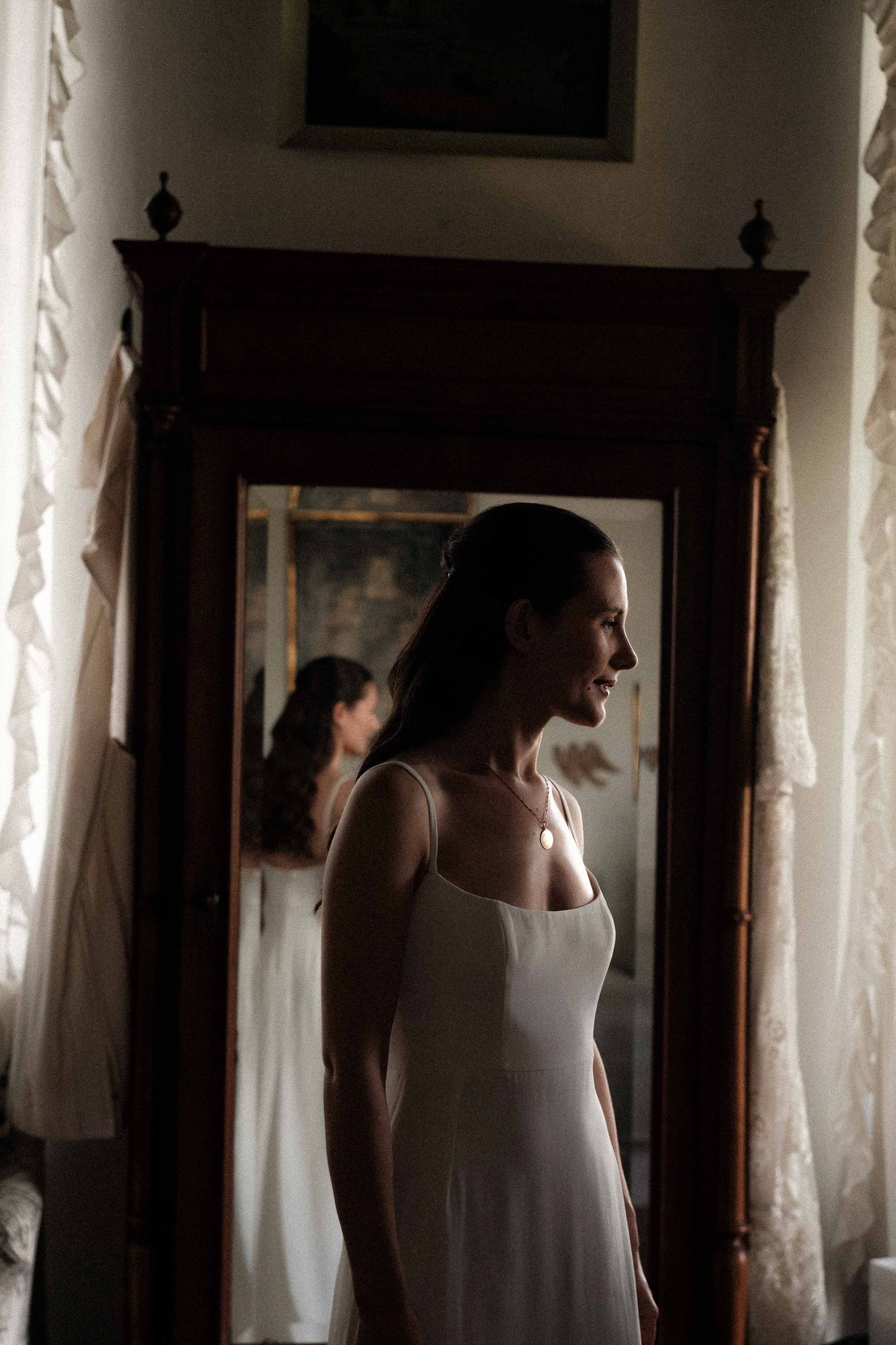 A series of four silhouetted figures stand near lace curtains in a dimly lit interior space.