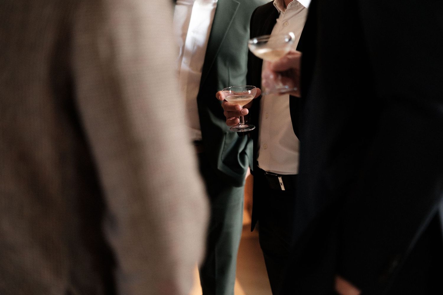 People holding cocktail glasses at a dimly lit social gathering or party.
