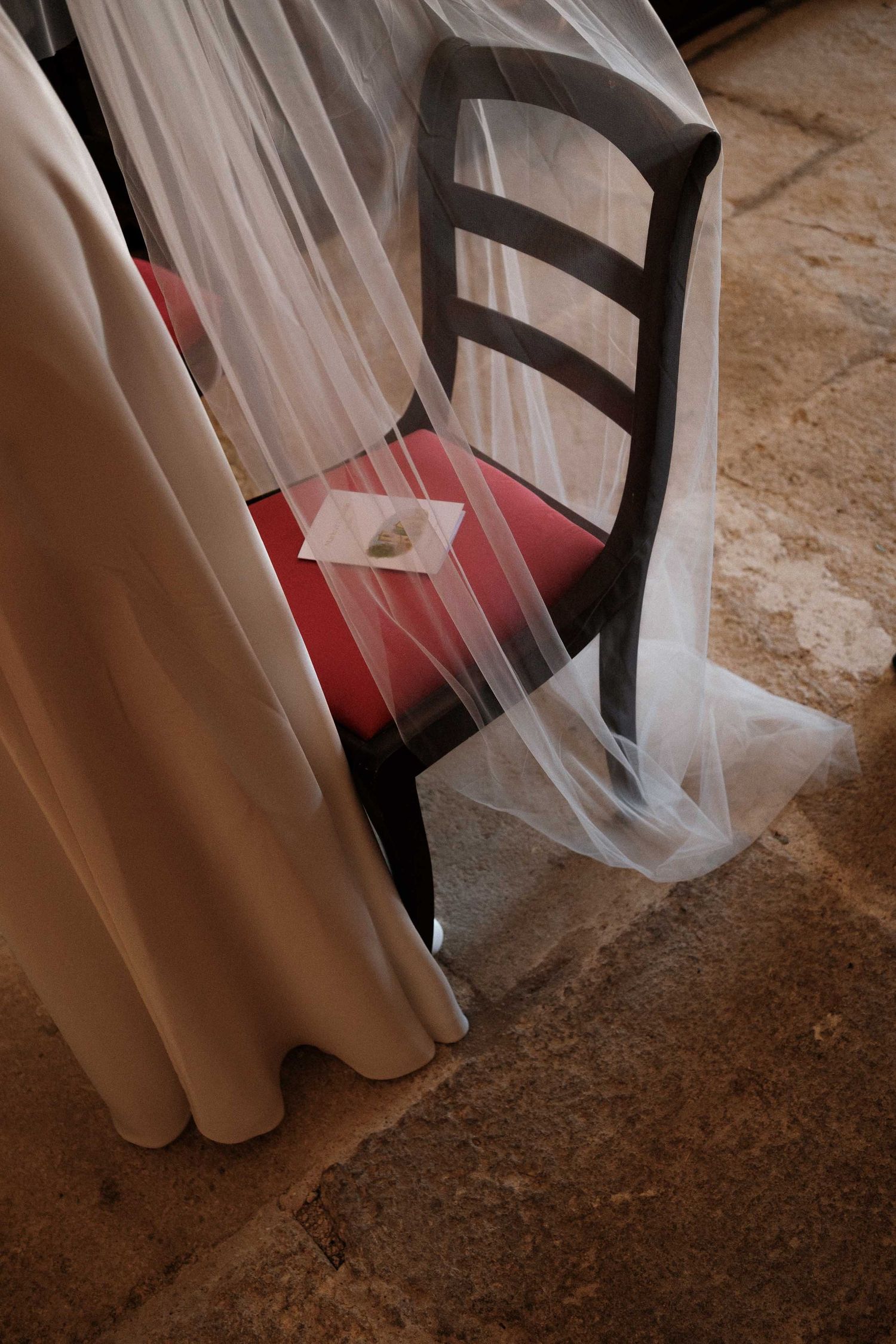 A flowing white wedding dress with red shoes peeking out from underneath against a stone floor.