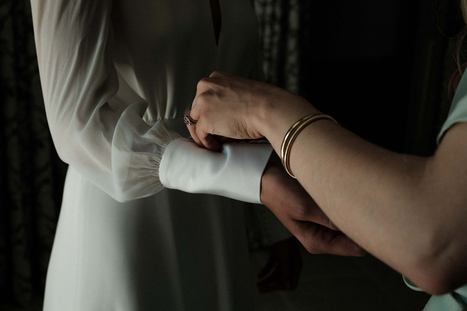 Close-up of hands gently holding a white fabric with delicate pleats and folds in soft lighting.