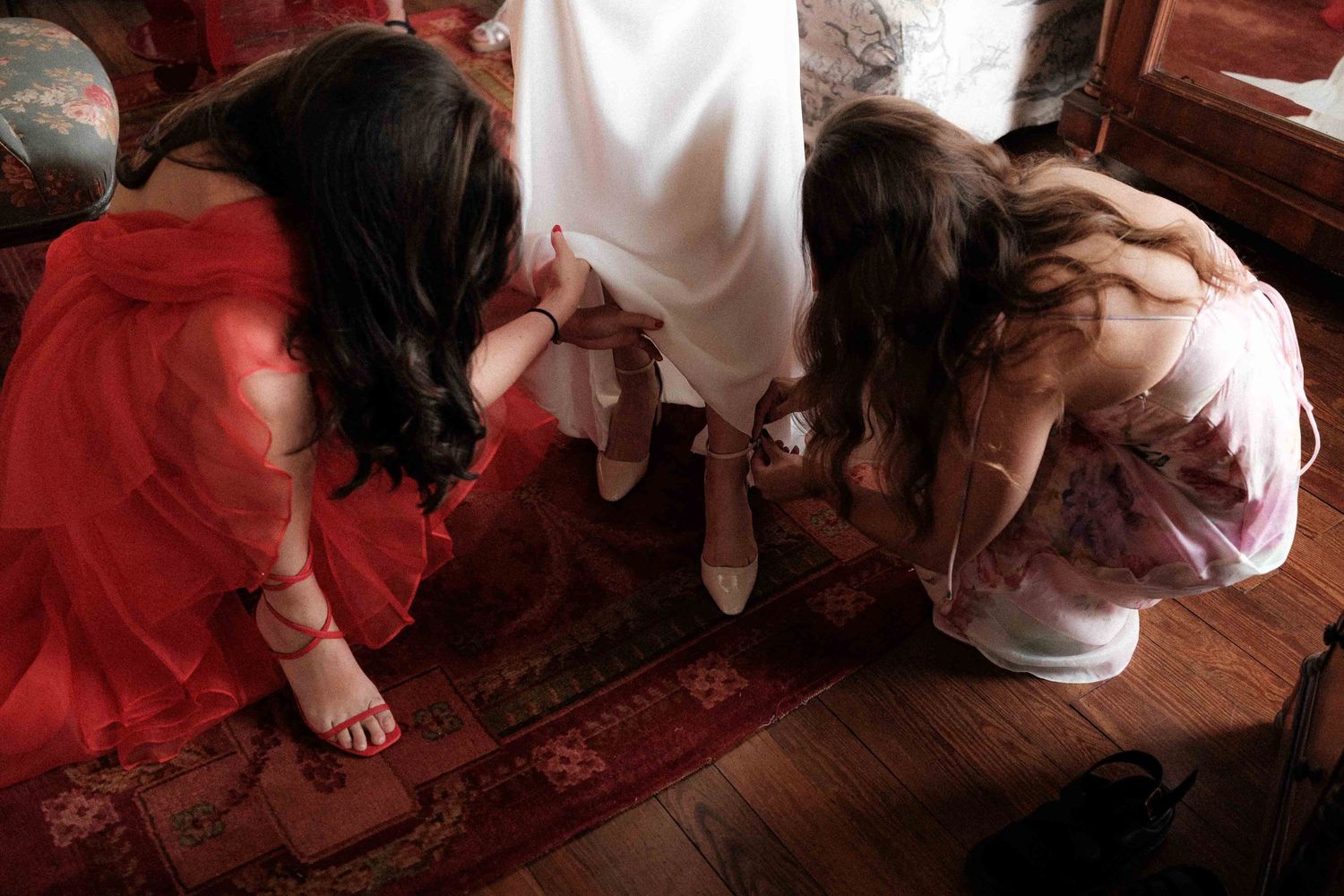 A bride getting ready with help adjusting her wedding dress and veil in a warm-toned setting.