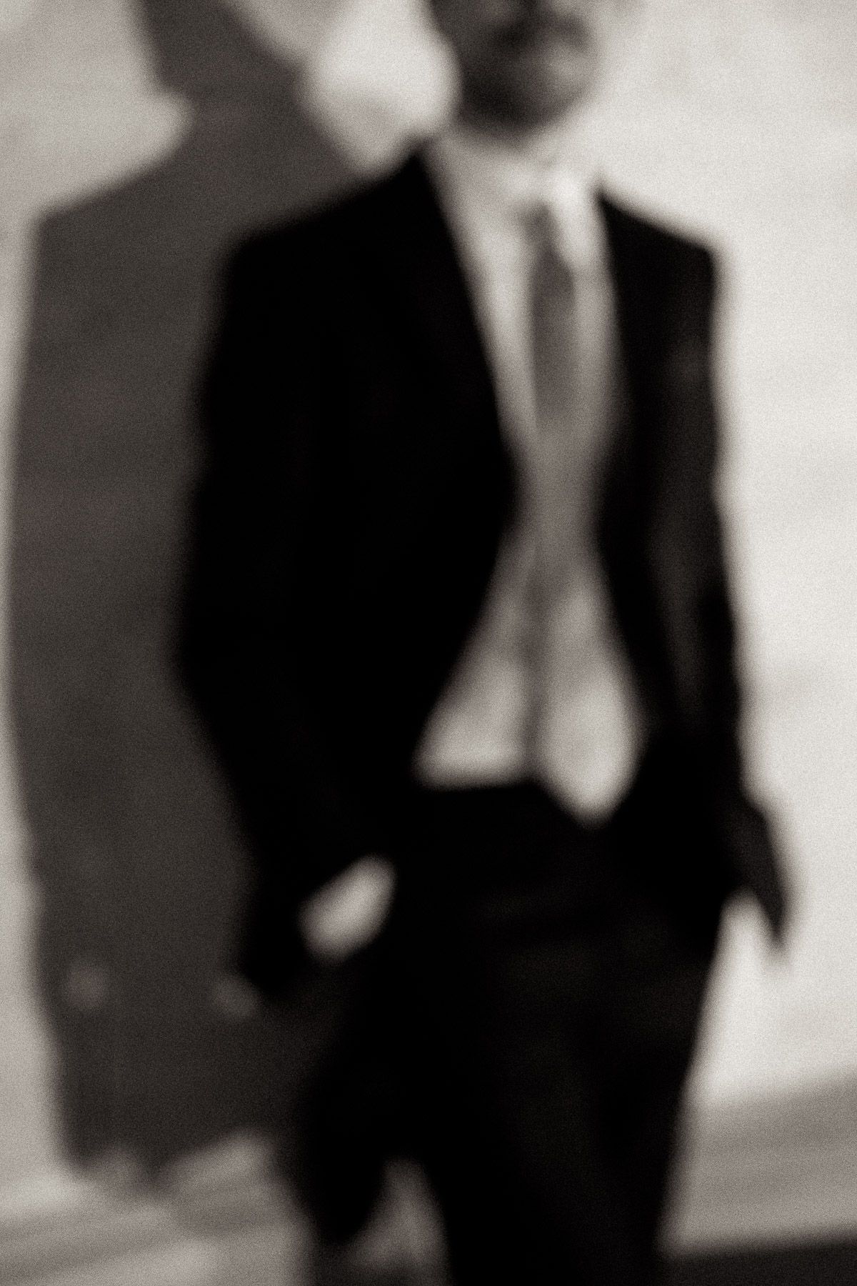A black and white photo shows three figures in dark suits standing together in a formal setting.