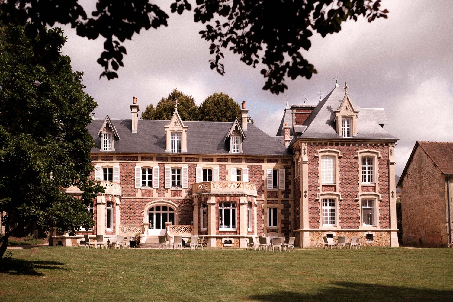 Panoramic view of a traditional French country estate with pink brick facade and manicured lawn in daylight.