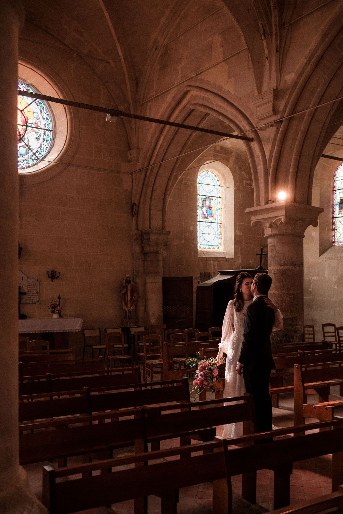 Interior of a traditional stone church with wooden pews and stained glass windows illuminated in warm light.