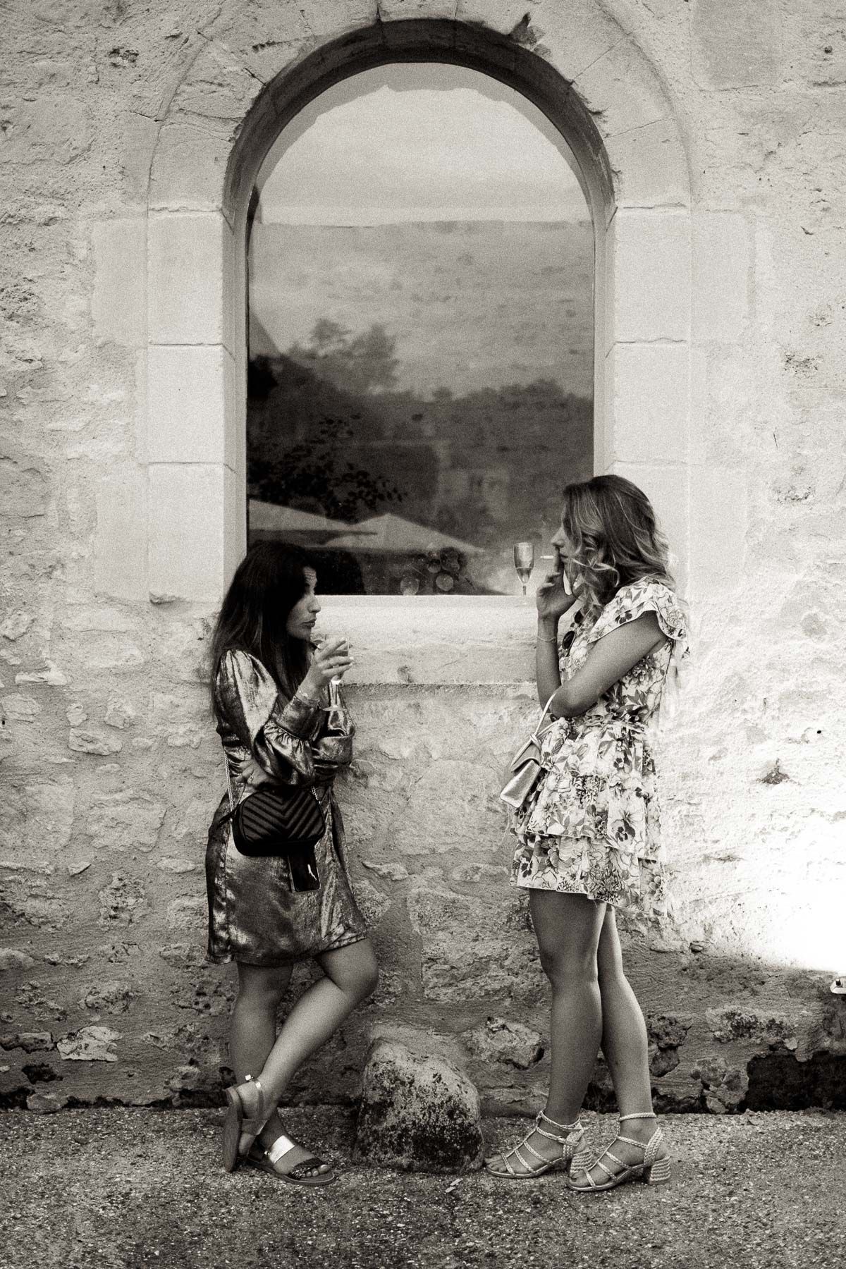 A black and white photo sequence showing two people playfully interacting through stone archways in a rustic wall.
