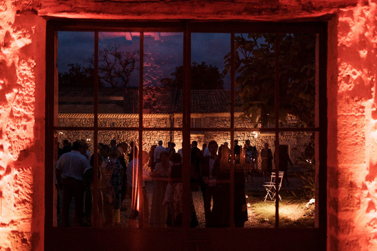 An outdoor wedding venue illuminated with dramatic red lighting against stone walls at dusk.
