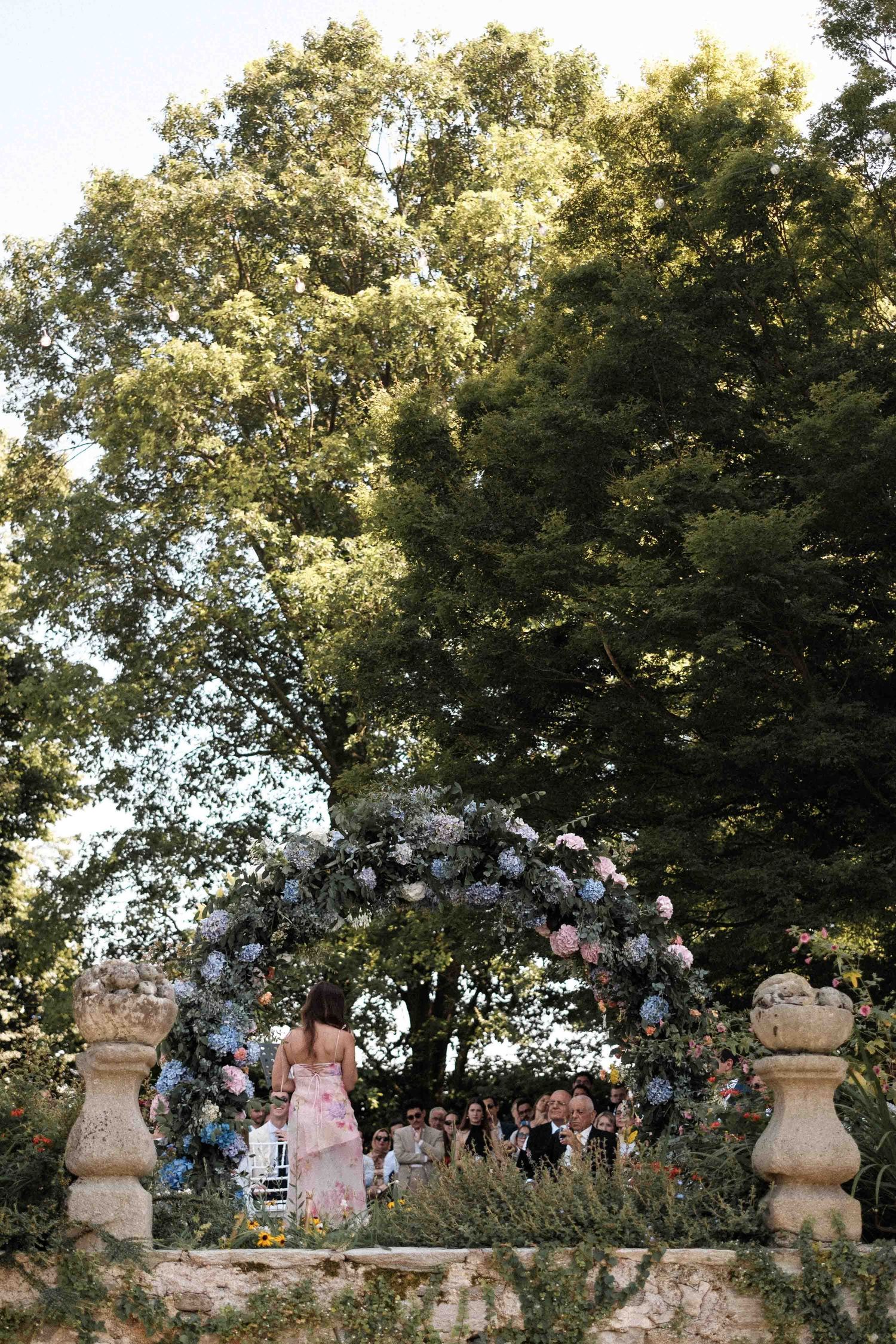 A series of outdoor wedding photos captured in a garden setting with trees and stone pillars at sunset.