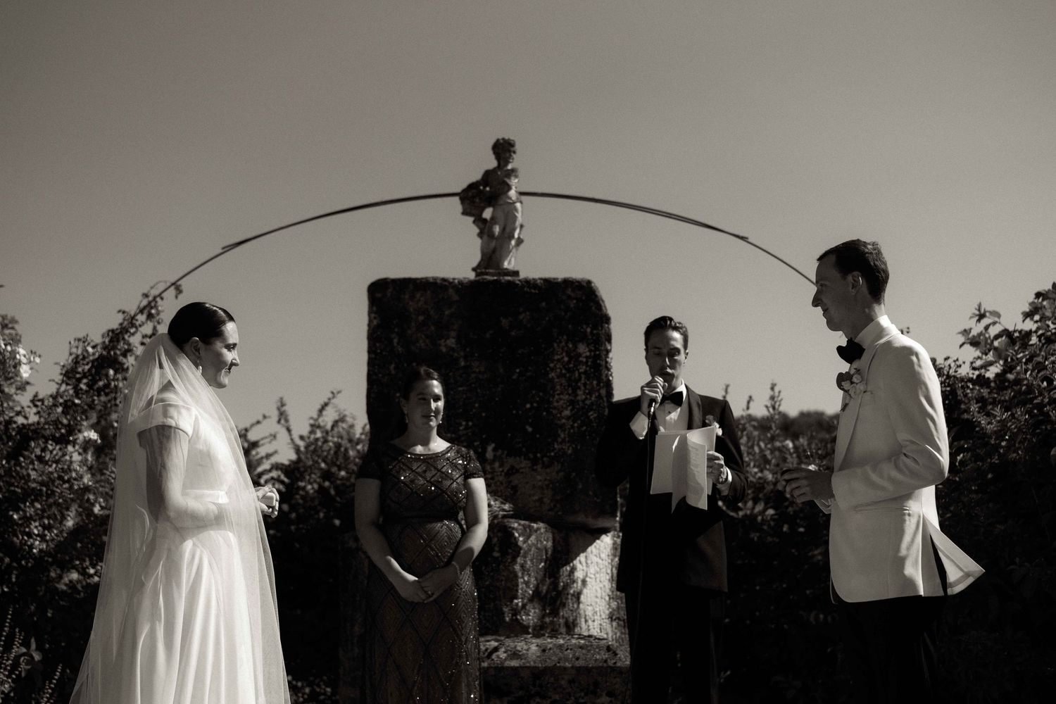 A black and white artistic wedding photo with a small figure silhouetted on top of a pillar with a curved line.