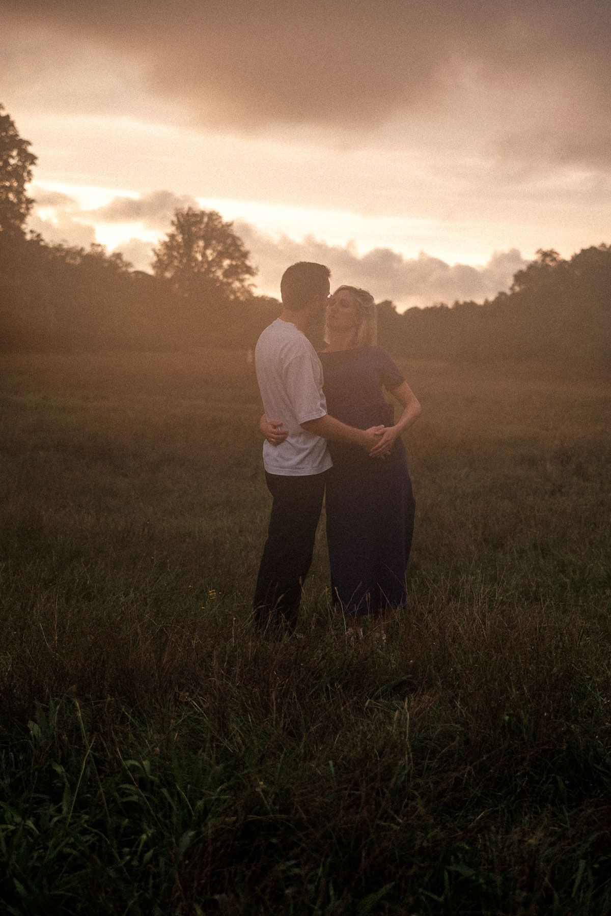 Two figures stand together in a misty field at sunset while golden light illuminates the tall grass around them.