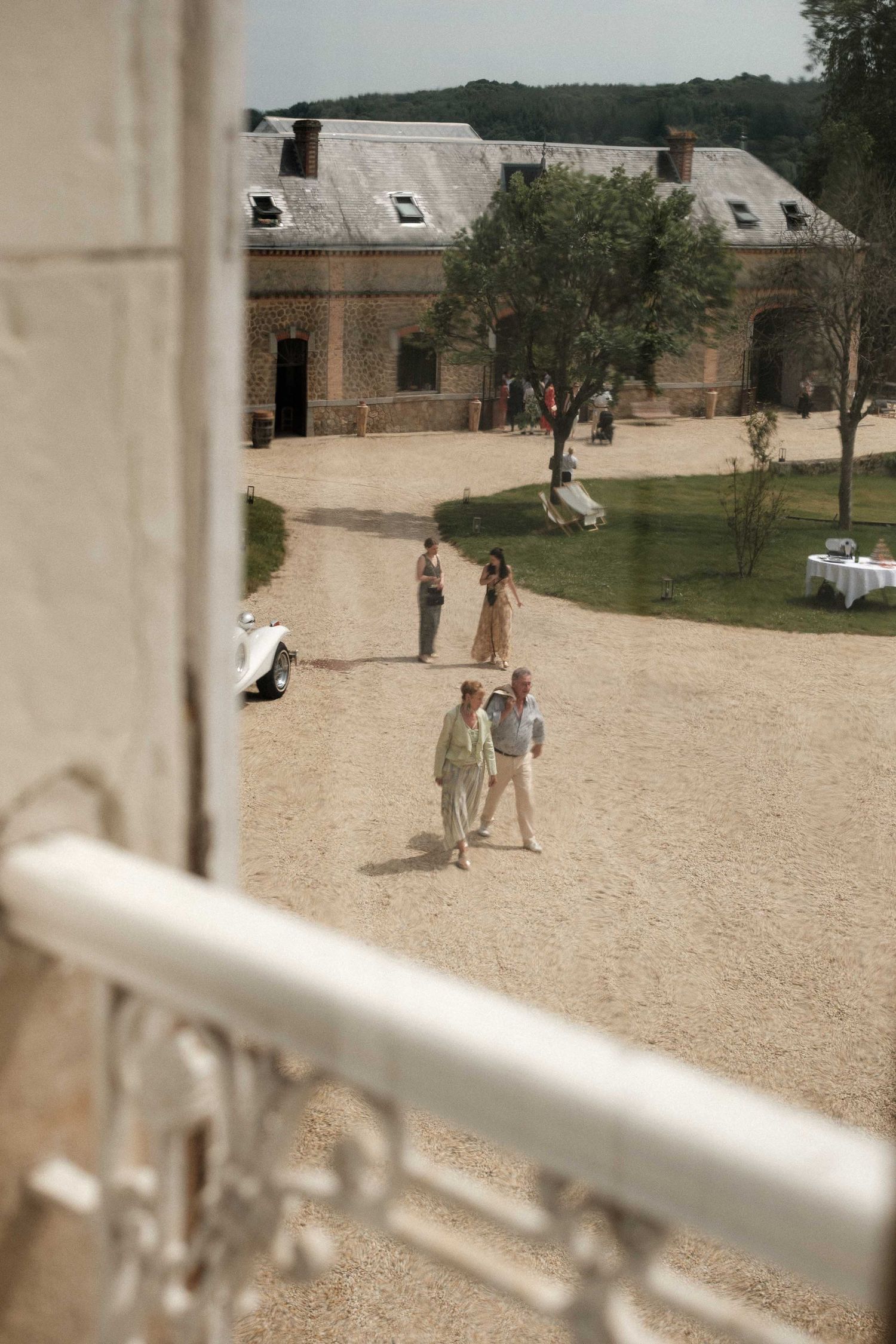 A sandy courtyard viewed through white railings with people and buildings visible in the distance.