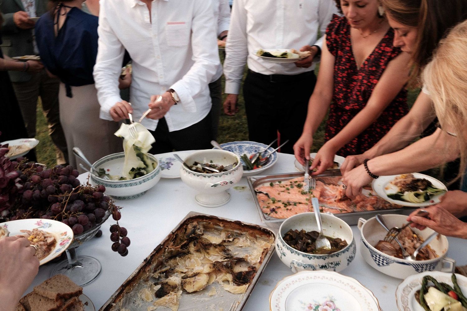 Hands reach for various dishes of food served at a formal dining event with white tablecloths.