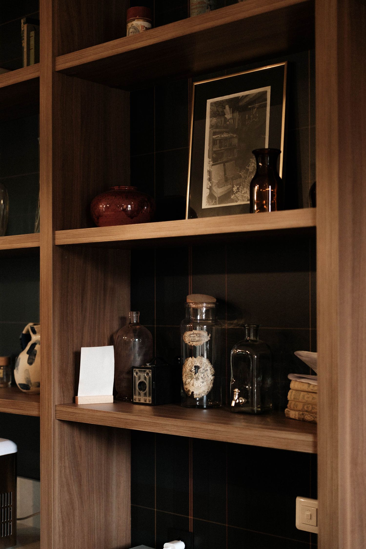 Wooden shelving unit with built-in compartments displays various glass jars and decorative items in warm lighting.