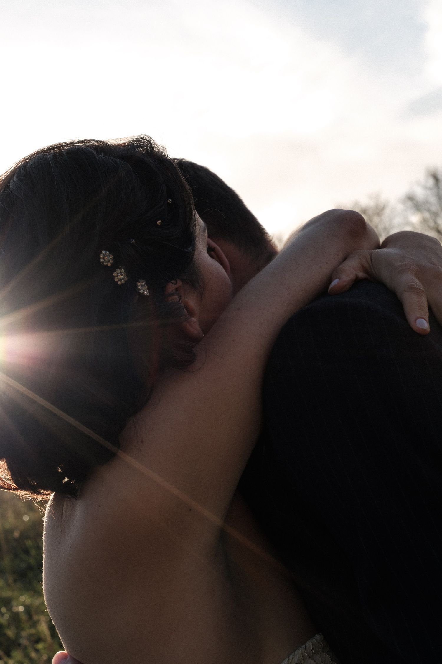 Silhouetted couple sharing a romantic kiss at sunset with sun flare creating a dreamy backlit effect.