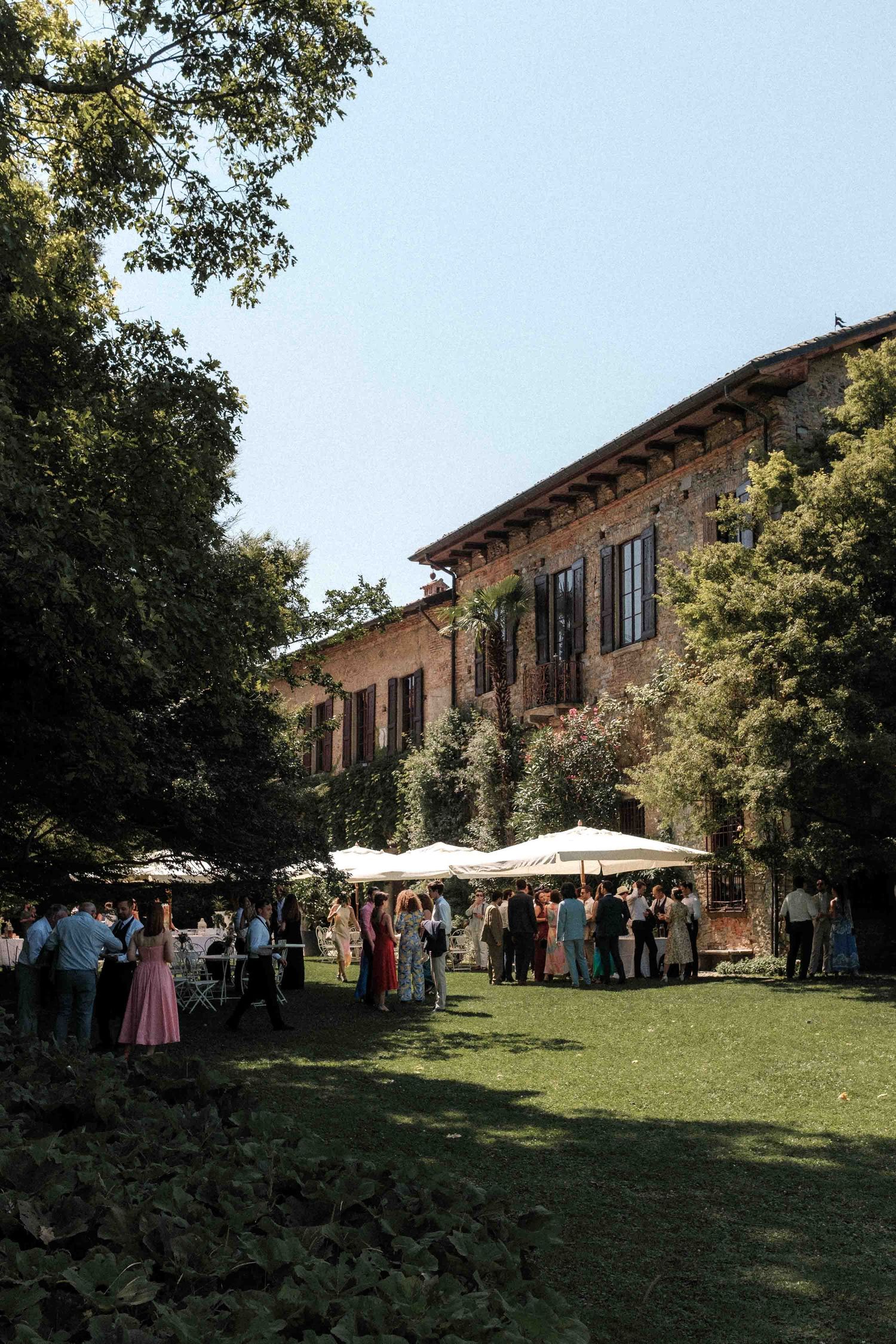 Rustic Italian villa with stone facade hosts outdoor wedding reception under blue summer sky.