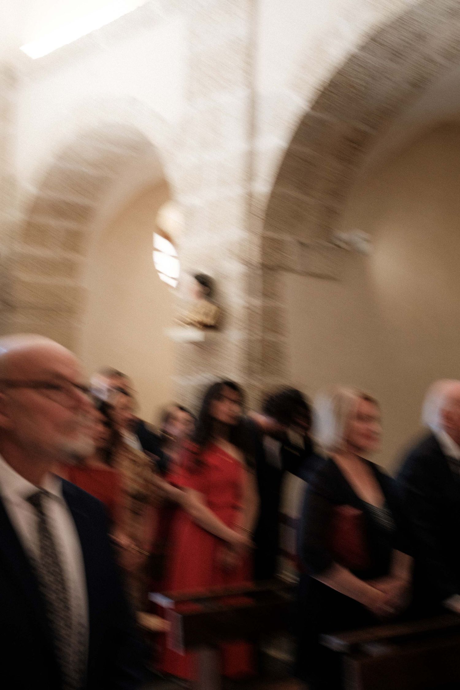 A motion-blurred image of people walking through an arched hallway with beige stone walls.