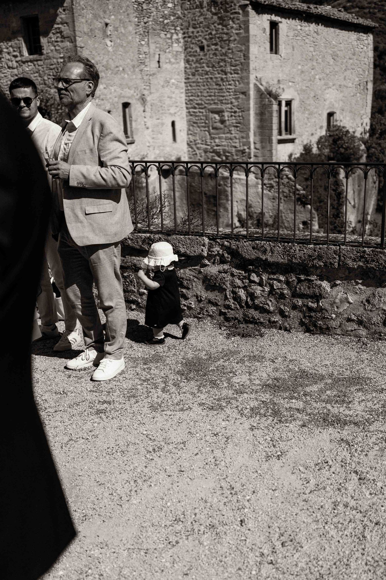 People walking along a stone wall path next to an old building in black and white photography.