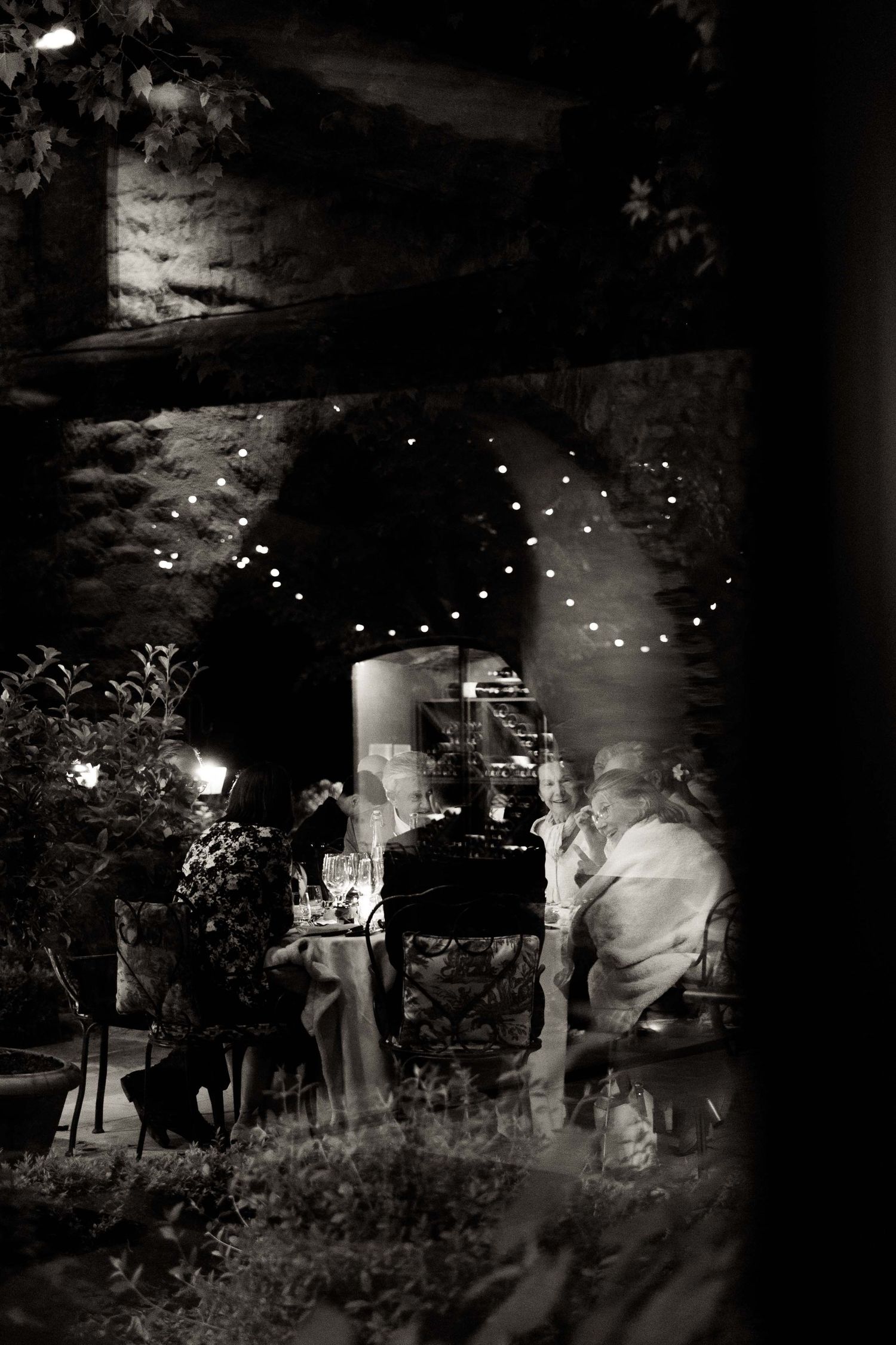 A dark nighttime scene shows silhouettes of people gathered around glowing lights in a wooded outdoor setting.