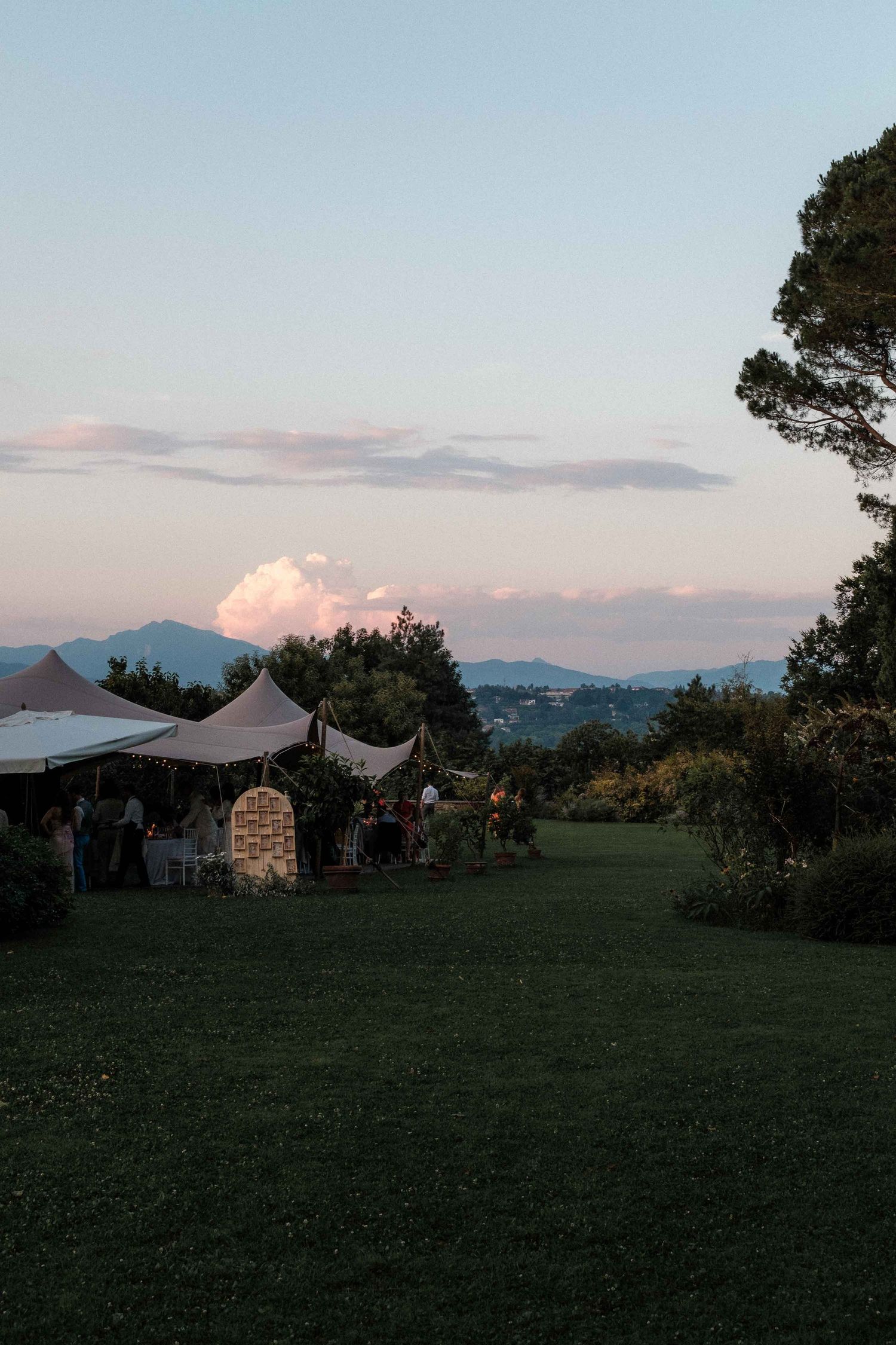 White event tents dot a grassy hilltop landscape at dusk with mountains visible in the background.