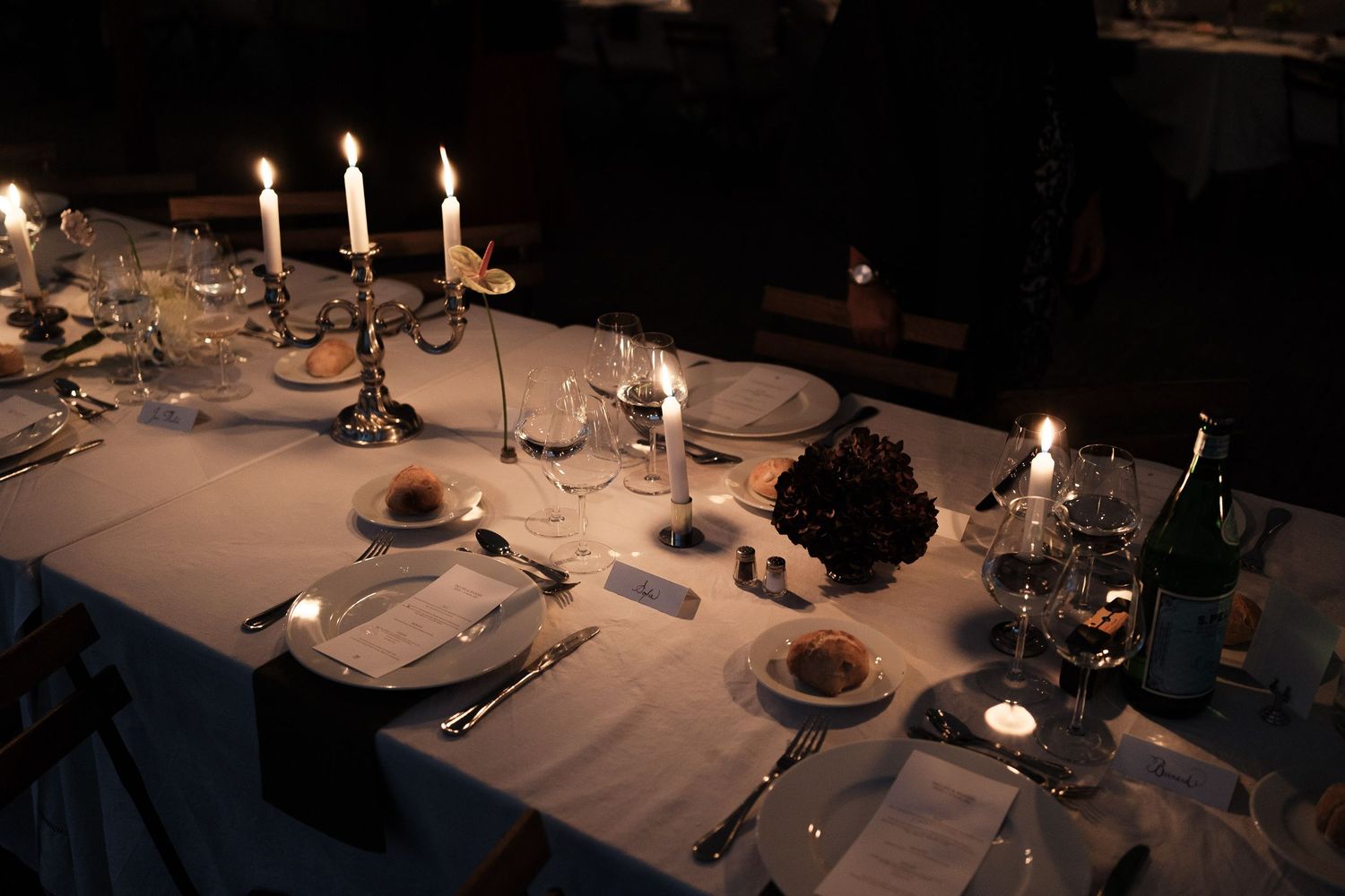 Elegant dining table settings with white linens and glowing candles create an intimate atmosphere in a dimly lit room.