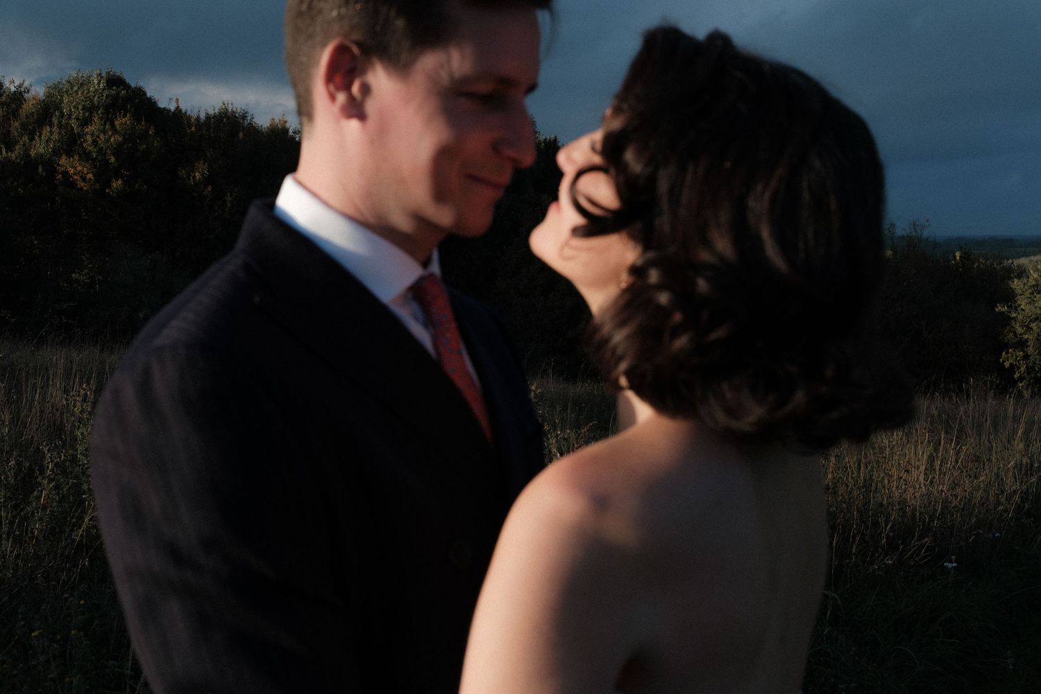 A romantic couple embraces in silhouette against a dusky outdoor setting during a wedding photo session.
