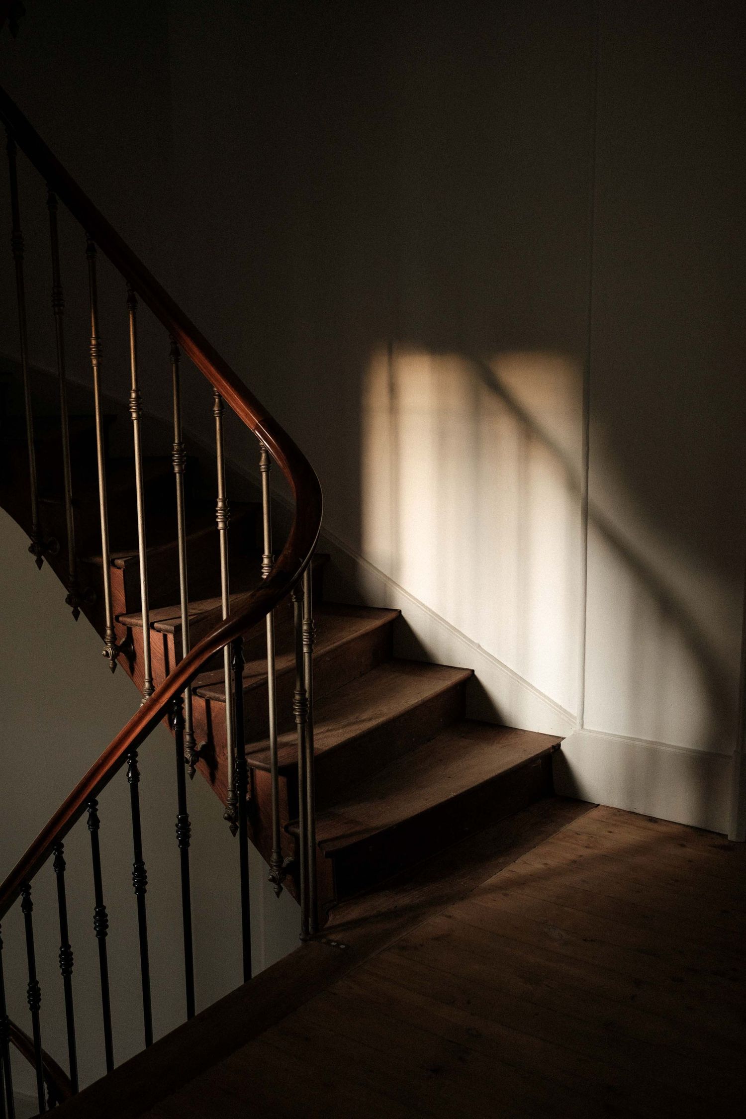 Dramatic shadows cast on a dark wooden staircase with metal railings in a dimly lit interior space.