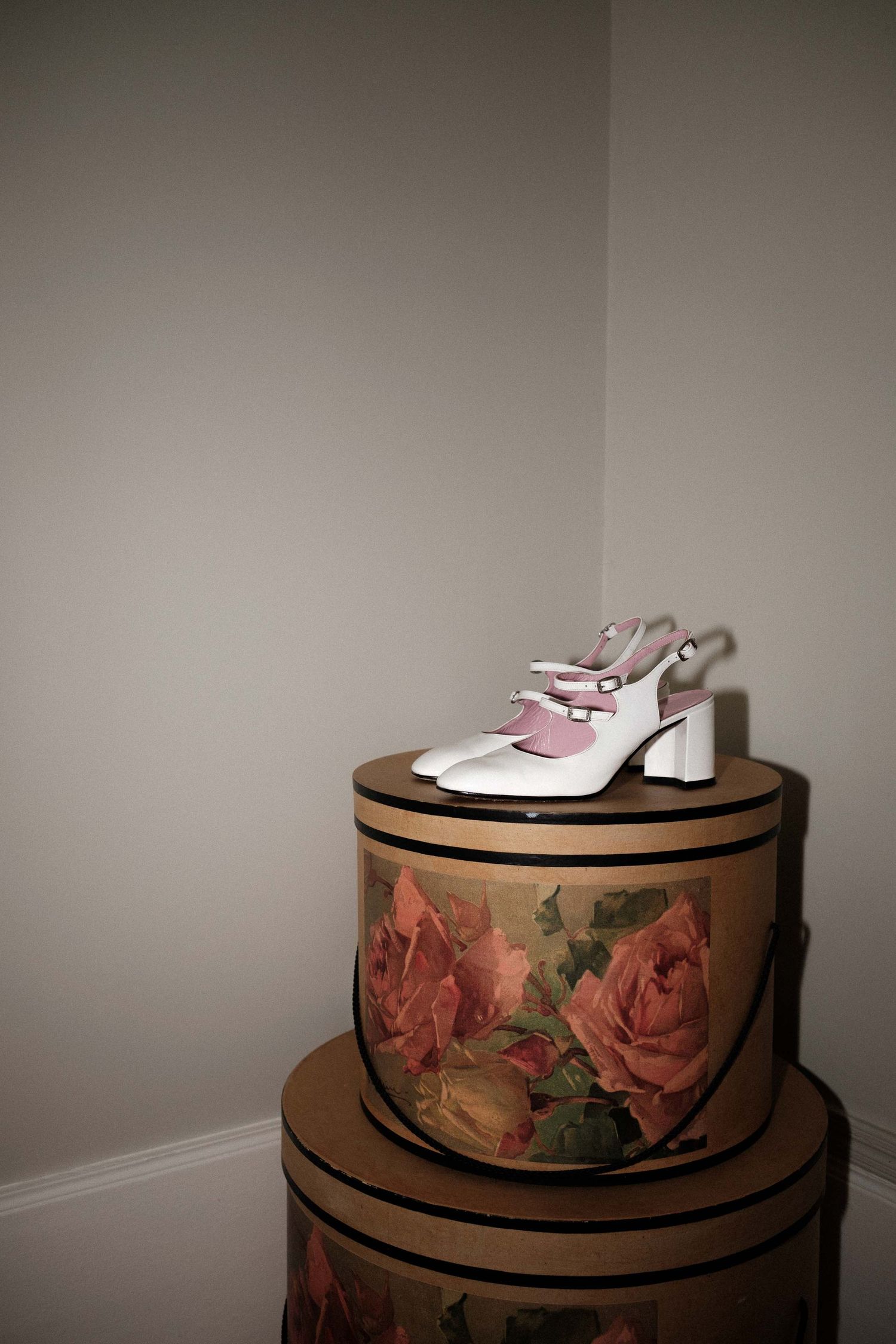 White slingback heels displayed on vintage floral hatboxes with rose designs in a corner setting.