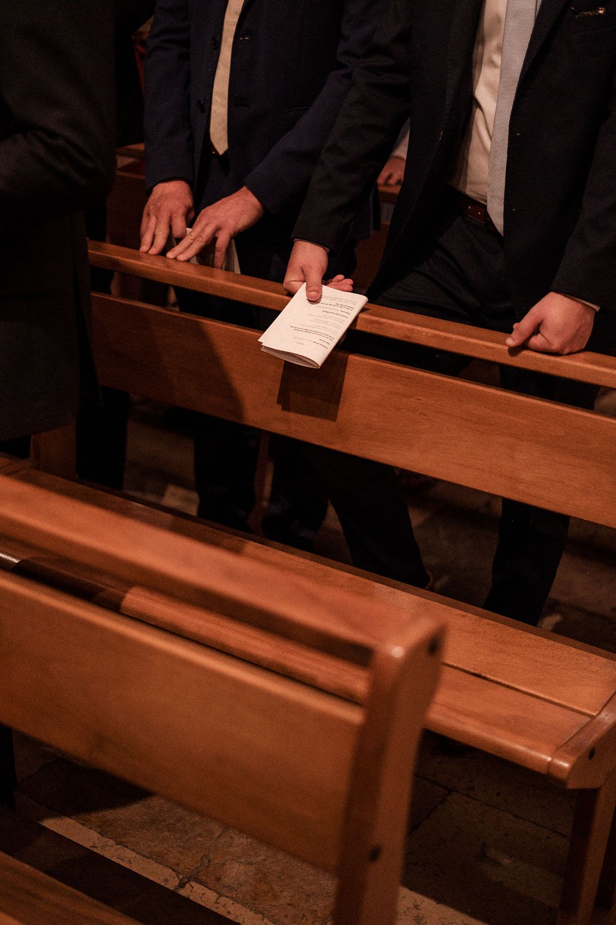 Hands holding papers while standing next to wooden church pews in a dimly lit interior space.