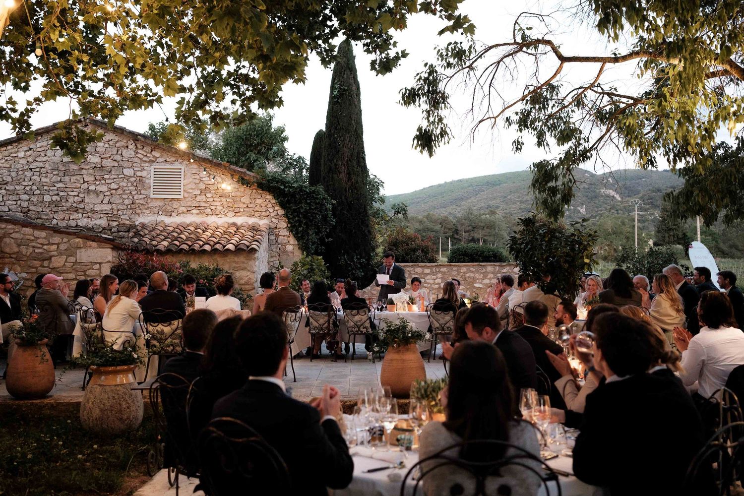 Rustic outdoor wedding reception setup with string lights and wooden tables at sunset.