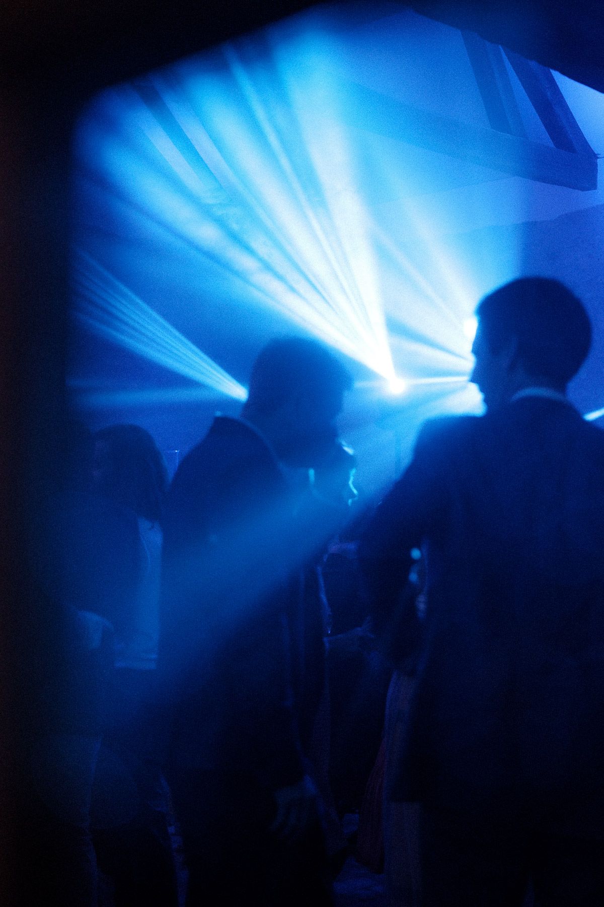 Silhouettes of people dancing in a nightclub with dramatic blue lighting and fog effects creating an atmospheric scene.