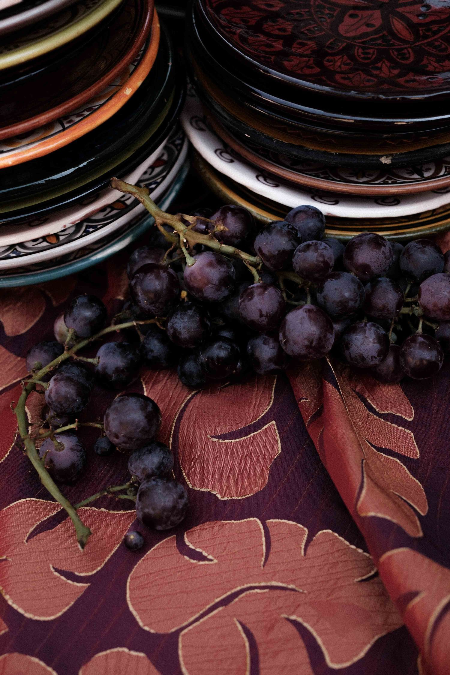 Fresh purple grapes and chocolate sandwich cookies arranged on a dark red textured surface with decorative elements.