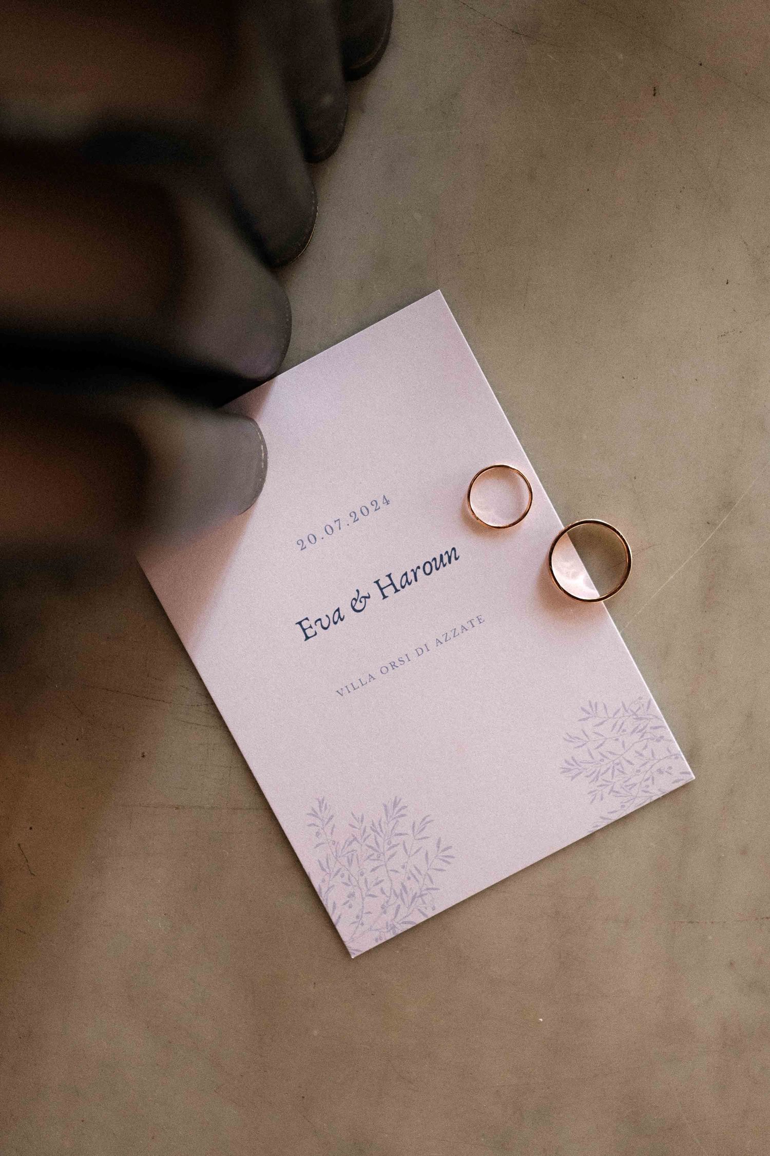 Wedding rings rest on delicate white invitation cards with purple floral designs and text in multiple artistic compositions.