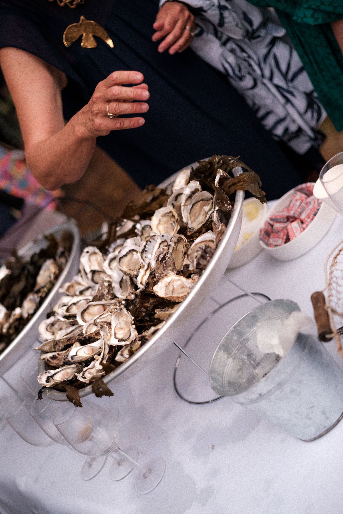 A plate of fresh oyster shells on ice with hands reaching for seafood at a restaurant table.