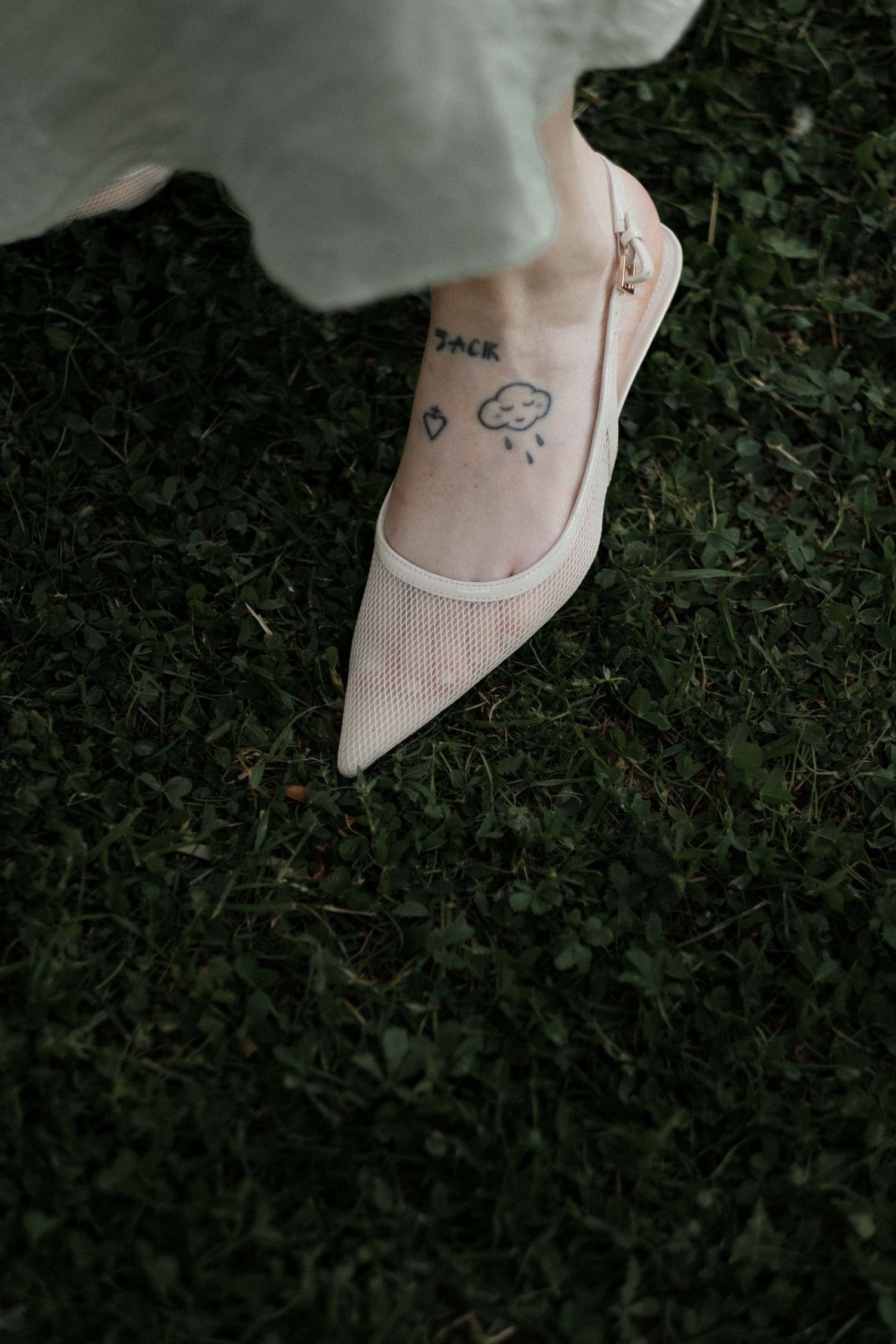 Close-up view of white ballet flats with delicate embroidered details on grass background.