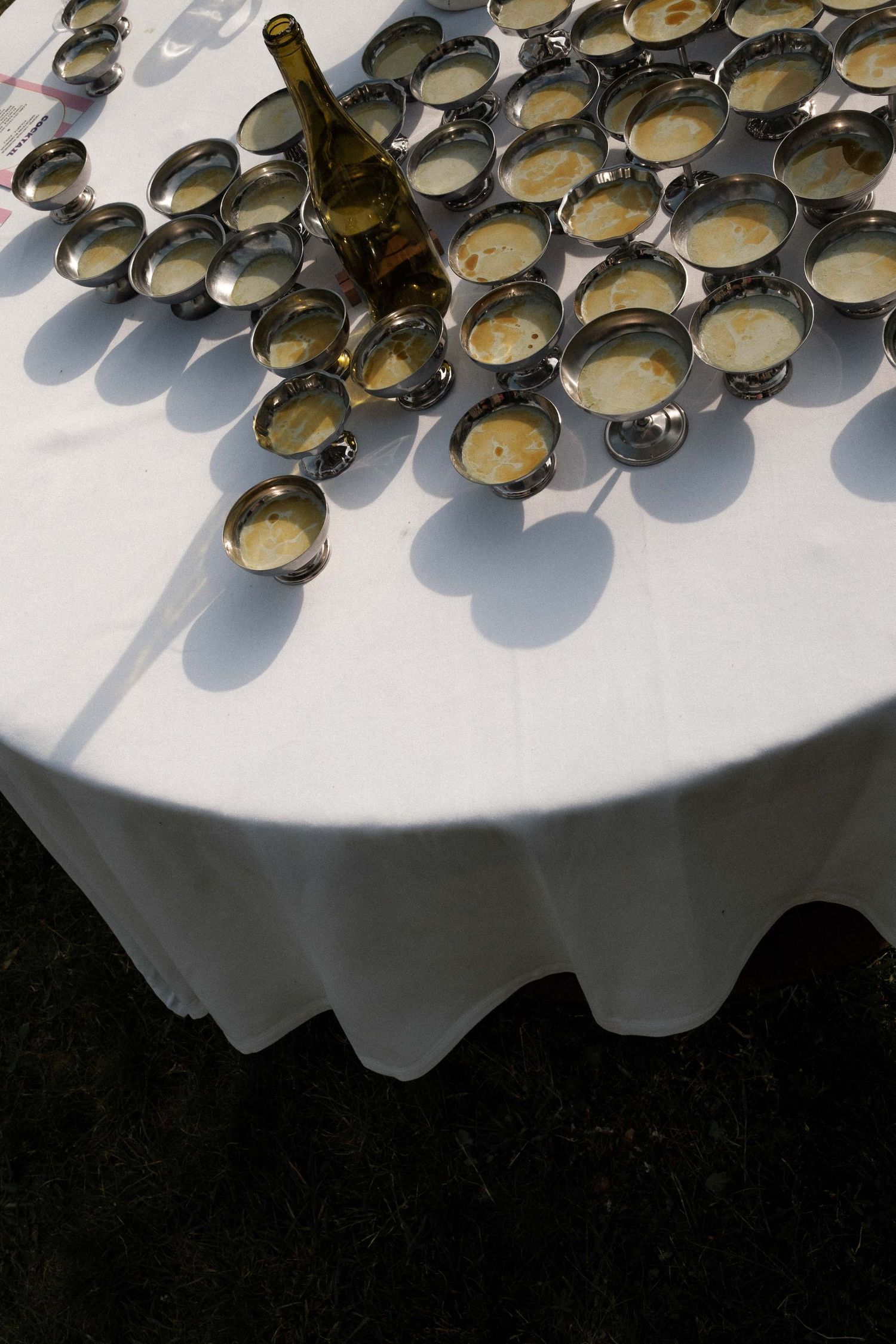 Multiple coffee cups and saucers arranged on a white tablecloth with dramatic shadows cast by sunlight.