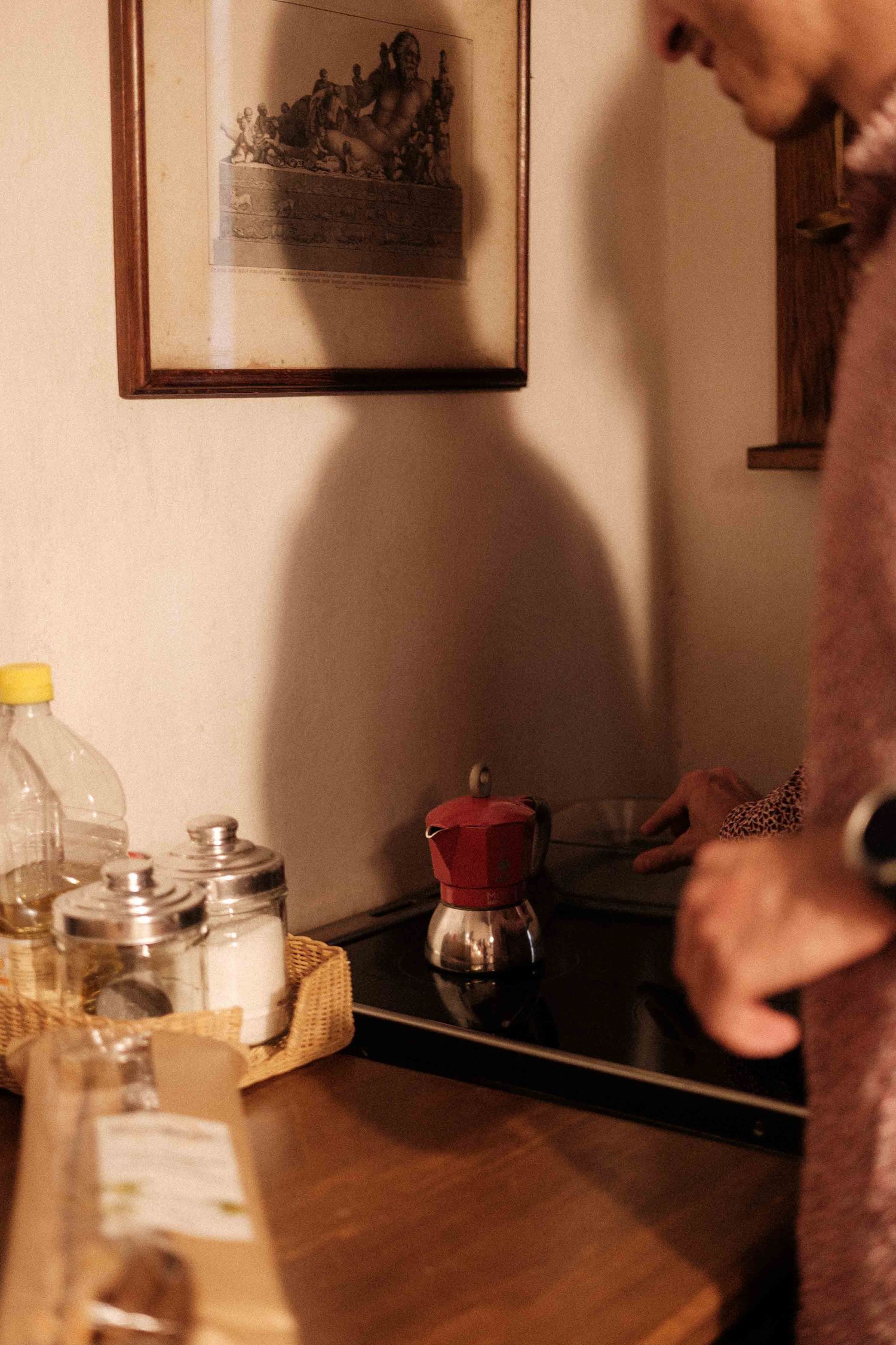 Warm-toned kitchen counter with glass jars and a red moka pot under framed artwork.