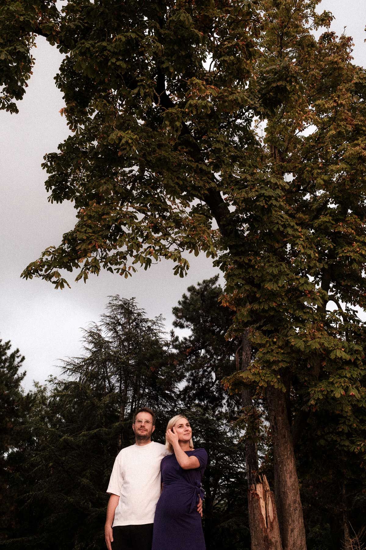 A couple shares a romantic moment together under tall autumn trees at dusk.