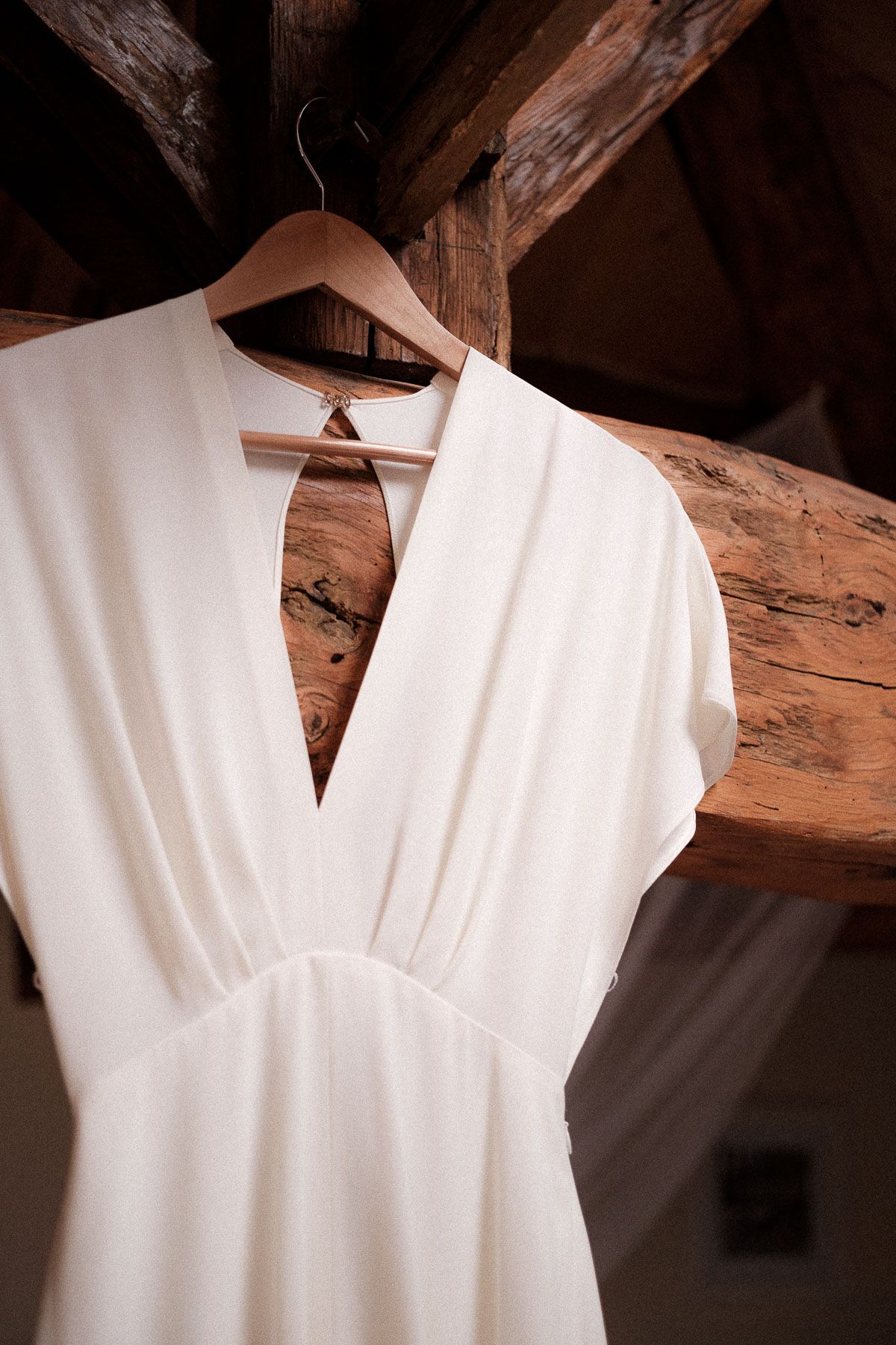 White sleeveless dress with v-neck neckline hanging on wooden beams against rustic background.