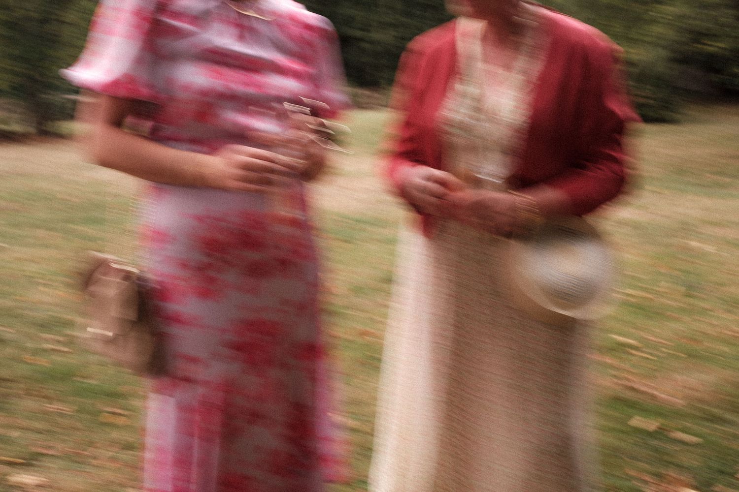 A person in a red and white floral dress walks through a garden setting with motion blur.