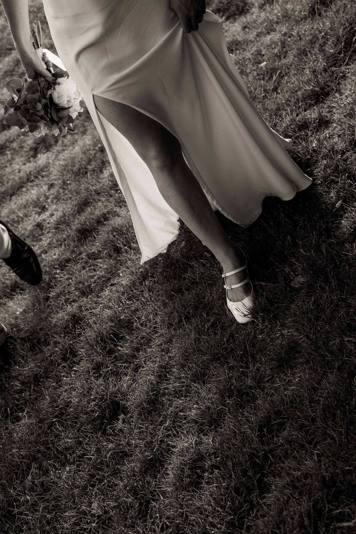 Black and white photo of a flowing dress and dress shoes on grass, with fabric caught in gentle motion.