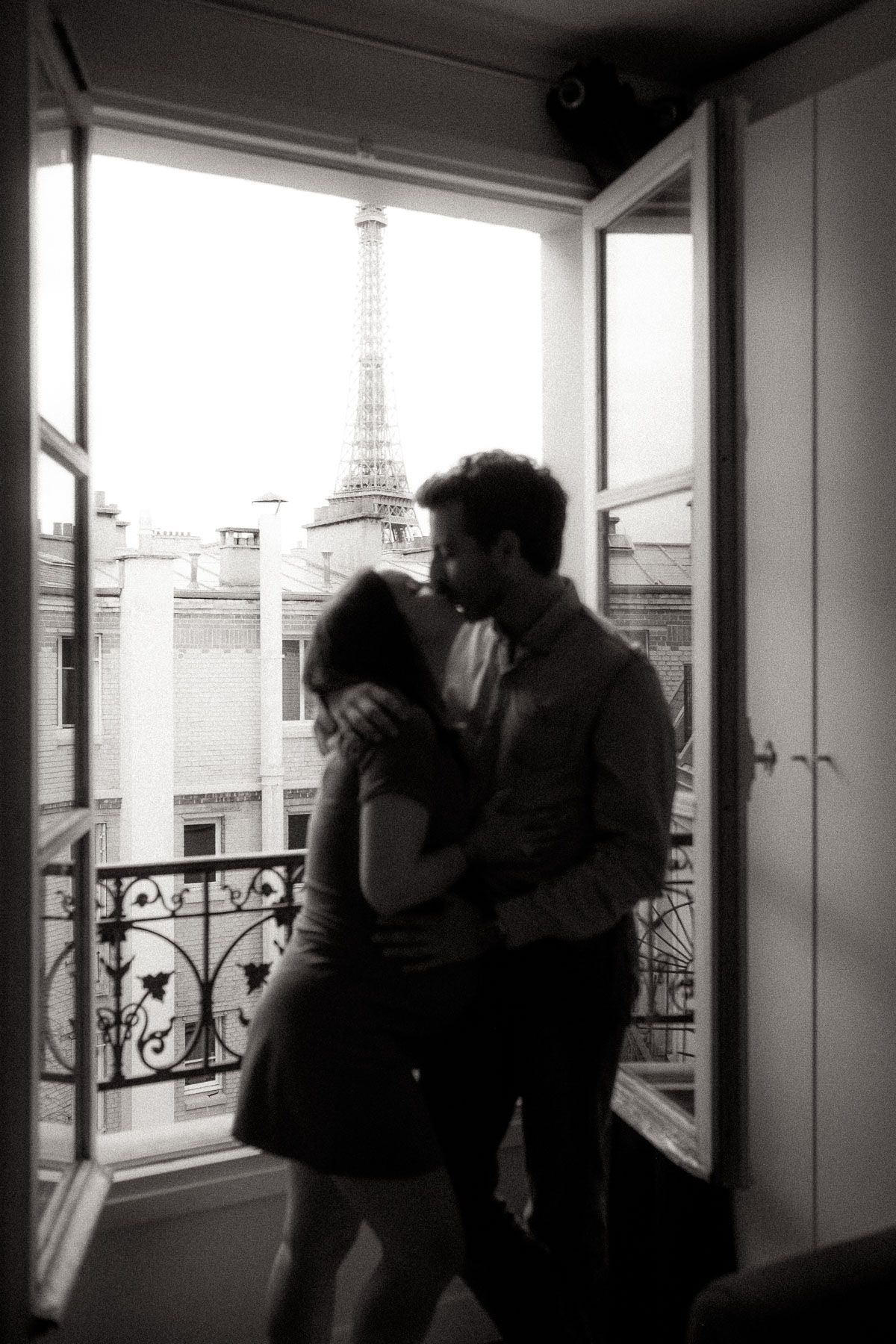 Silhouettes of two people embracing by a window with the Eiffel Tower visible in the background.