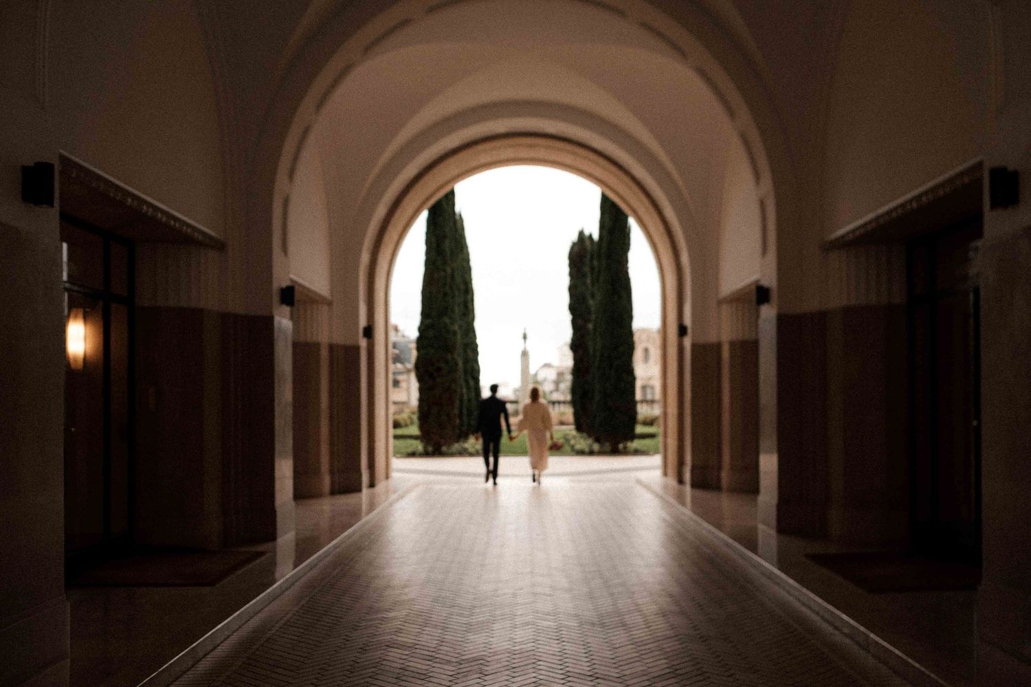 A silhouetted figure stands in an arched hallway with cypress trees visible through the opening.