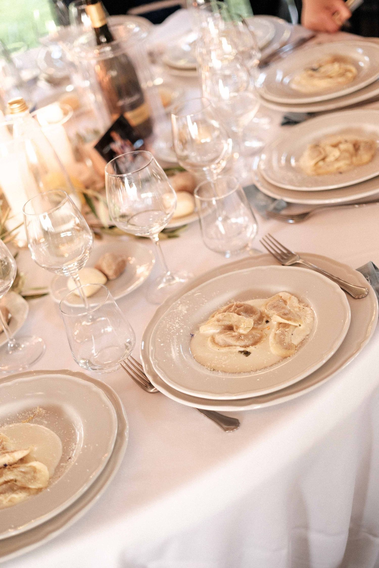 Multiple place settings with white plates and wine glasses on an elegant white tablecloth at a formal dining event.