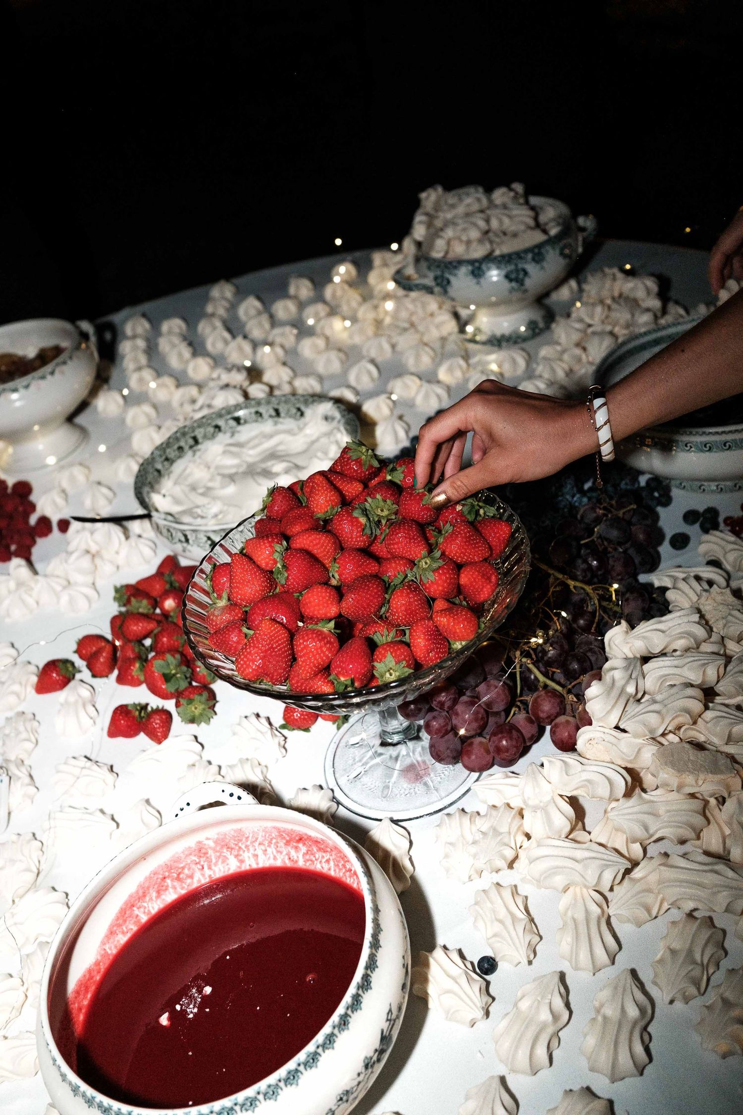 Fresh strawberries and meringues arranged on a dessert table with a bowl of red sauce for dipping.